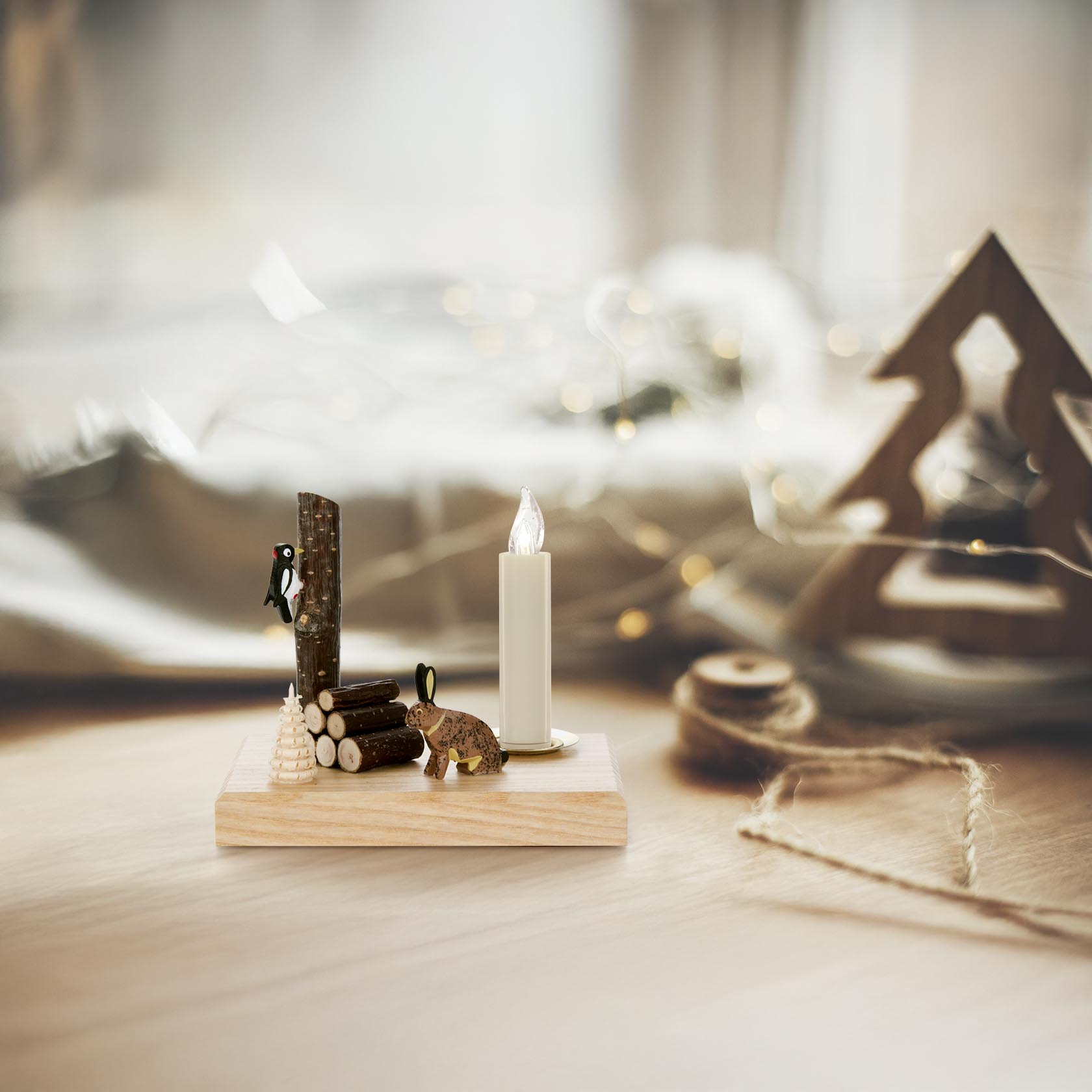 Ein dekorativer Kerzenhalter aus Holz mit einem geschnitzten Hasen und einem Specht, der auf einer kleinen Baumstammnachbildung sitzt. Geeignet für Kerzen mit 14mm Durchmesser.