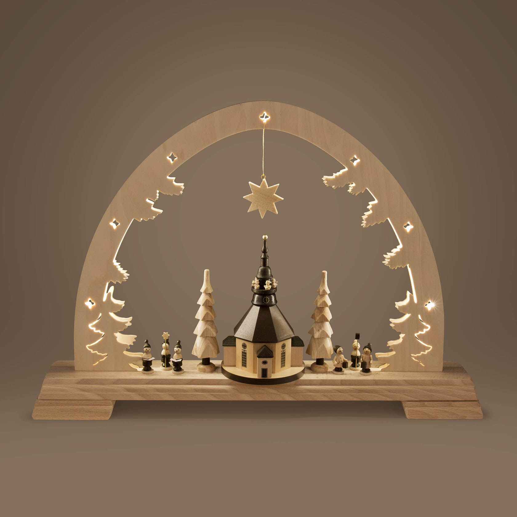 Schwibbogen aus Holz mit beleuchteter Seiffener Kirche in der Mitte, umgeben von zwei Bäumen und kleinen Figuren, LED-beleuchtet, auf Holzsockel.