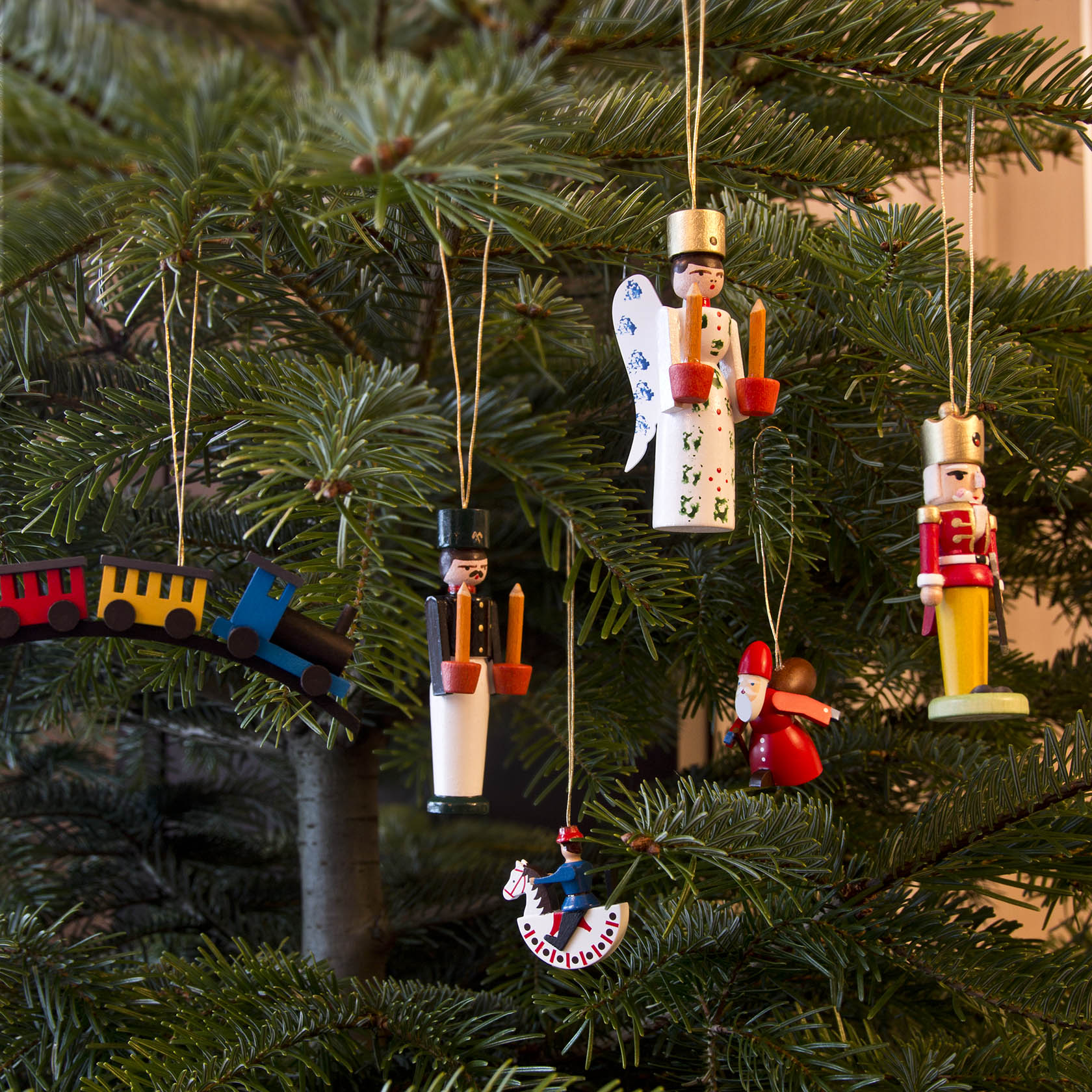 Ein Weihnachtsbaum mit Holzornamenten, darunter ein Engel und ein Bergmann, beide mit Kerzen in den Händen, sowie ein bunter Zug und ein Schaukelpferd.