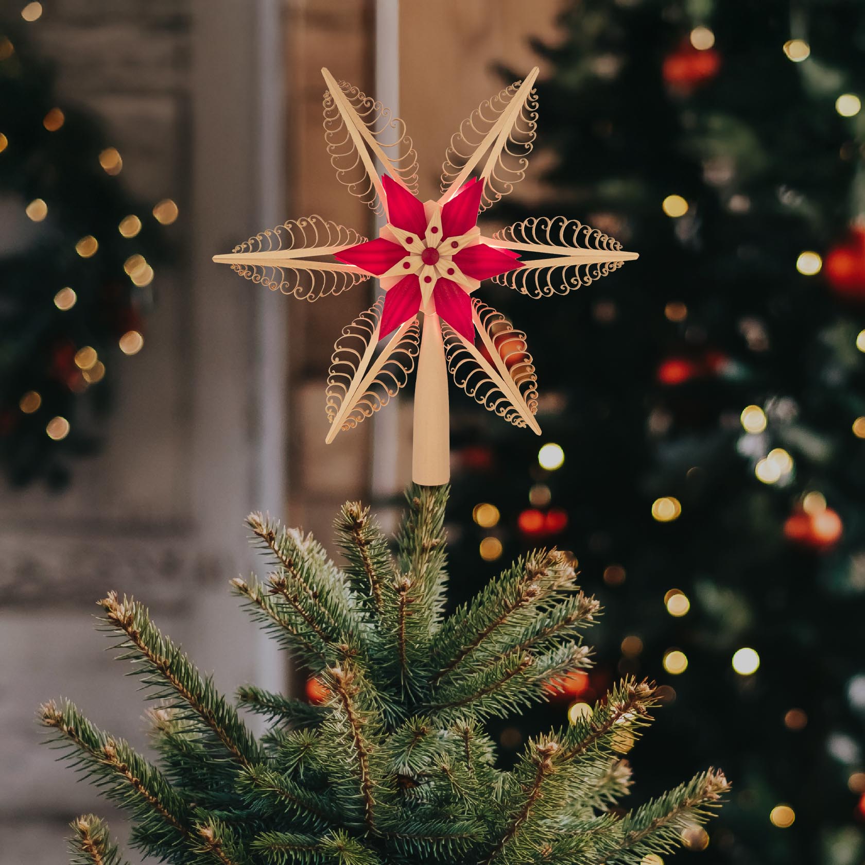 Ein traditioneller Spanstern in Rot und Naturfarben mit elektrischer Beleuchtung, als Christbaumspitze auf einem Weihnachtsbaum.