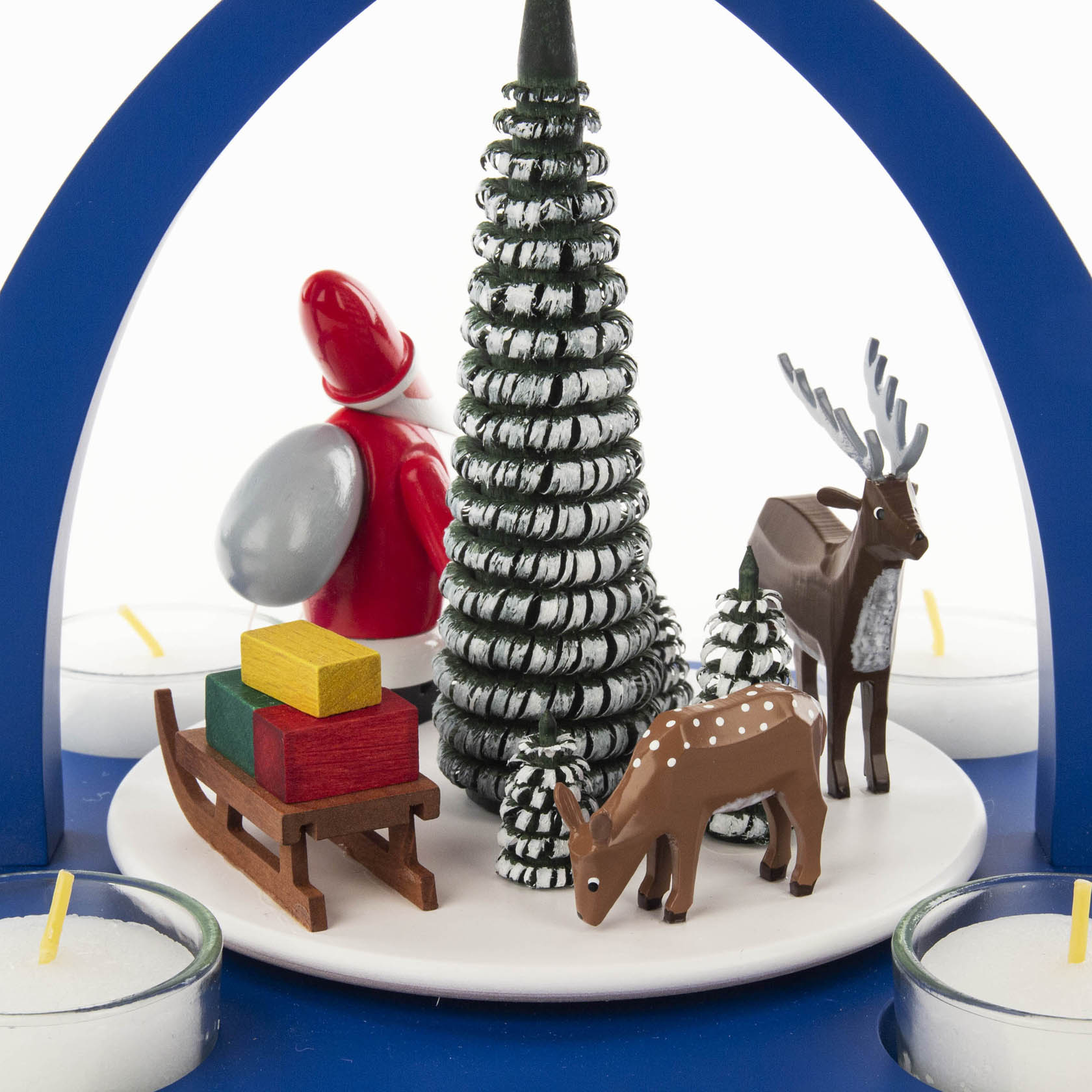 Dekoration mit Weihnachtsmann-Figur, Rentier, Reh und zwei schneebedeckten Tannenbäumen. Ein roter Schlitten mit bunten Geschenken, umgeben von Teelichtern.