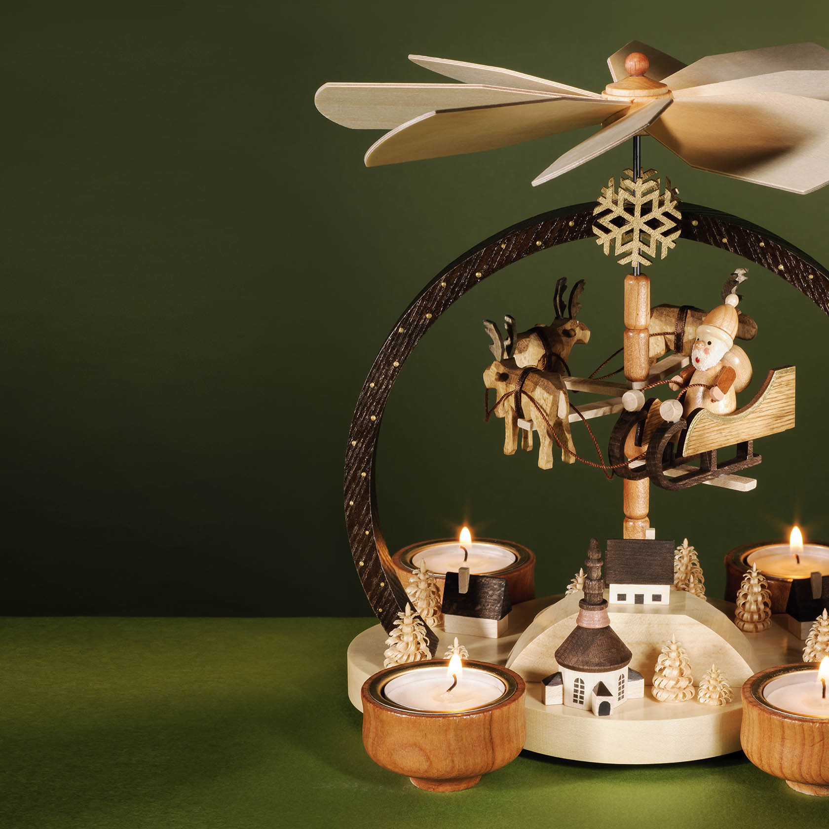 A wooden Christmas pyramid with a Santa figure in a sleigh pulled by reindeer, surrounded by tea lights. The heat makes the top fan spin.