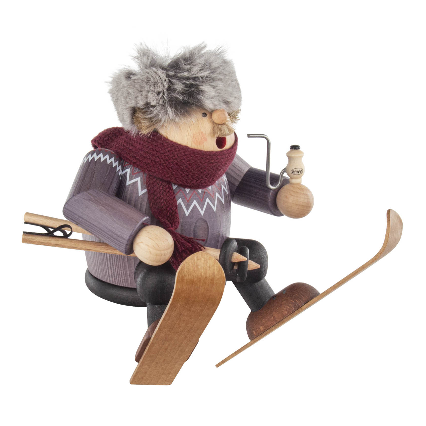 Ein Räuchermann als Skifahrer mit Pelzmütze, rotem Schal und Ski in der Hand. Er sitzt auf einer Kante und hält eine Pfeife.