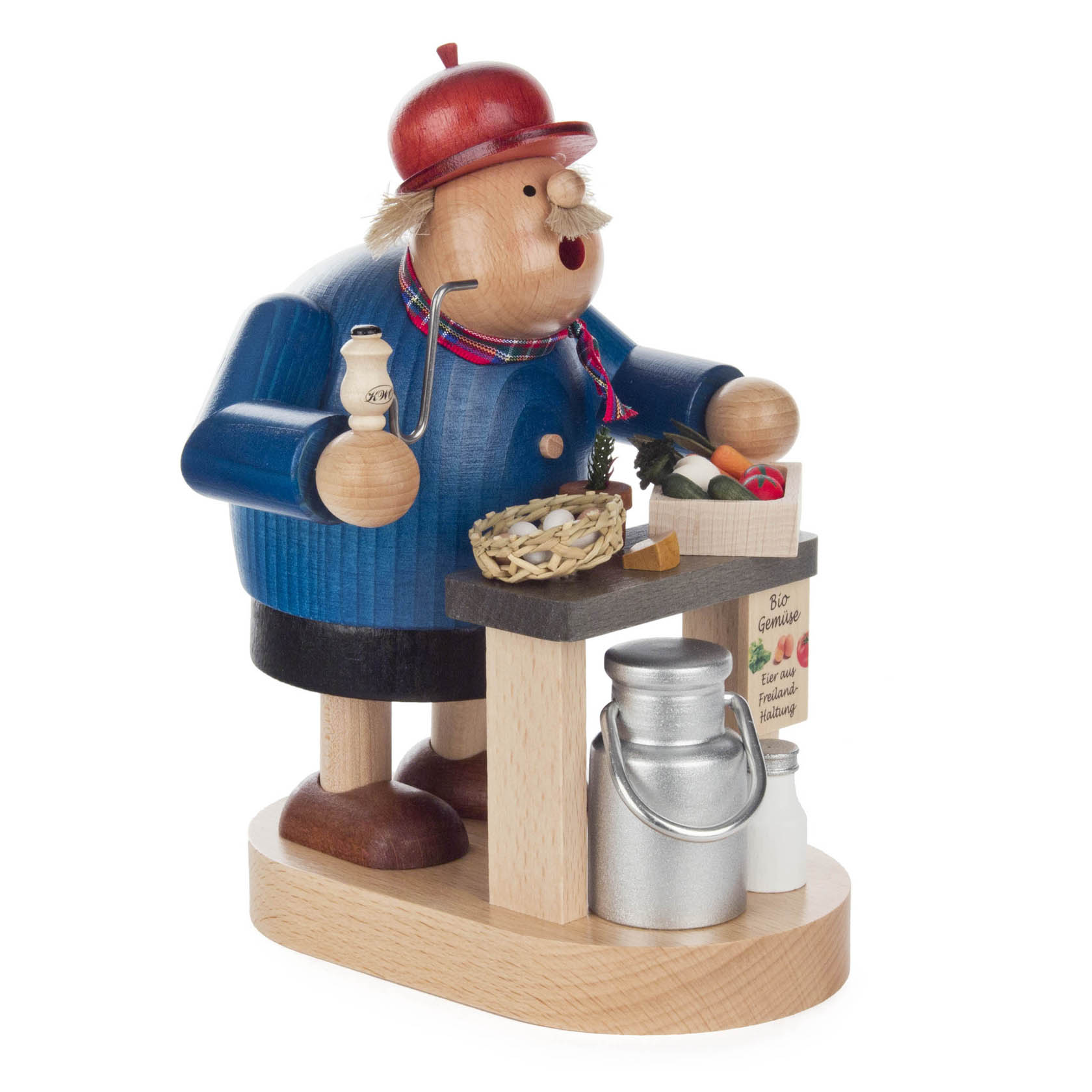 Holzfigur eines Räuchermanns, dargestellt als Bio-Bauer mit roter Mütze, blauem Mantel und gemusterter Mütze. Er hält ein Säckchen und steht neben einem Tisch mit Obst und Milchkanne.