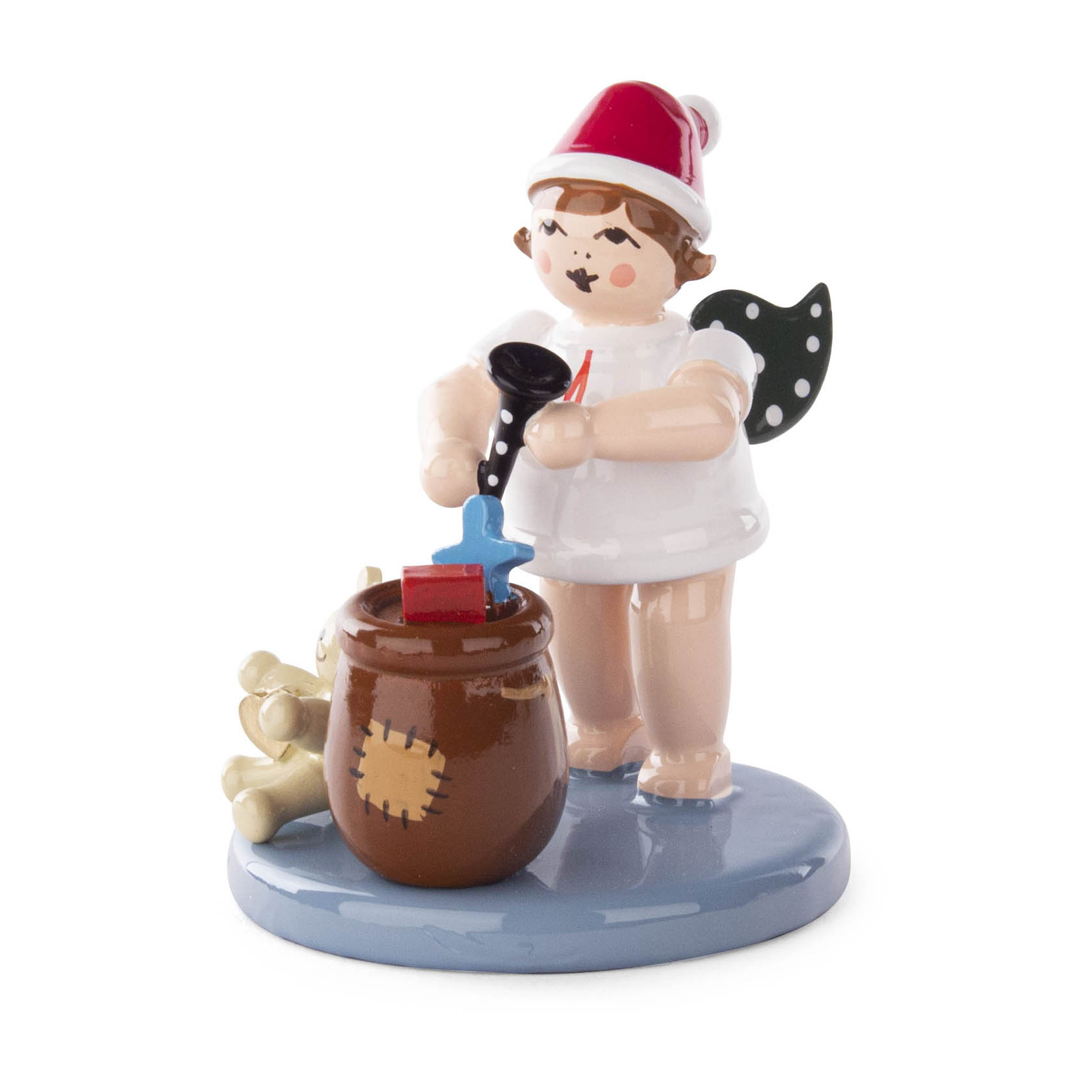 A ceramic angel figure with a red Santa hat, holding a black trumpet, standing next to a brown sack filled with gifts, including a teddy bear. im Dregeno Online Shop günstig kaufen
