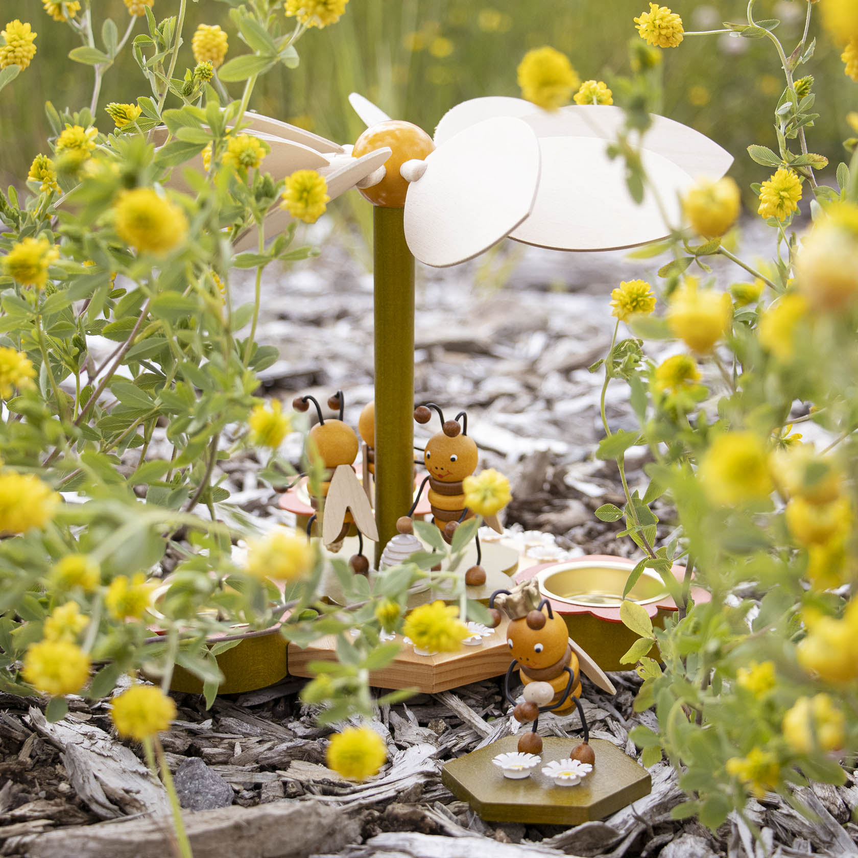 Dekorative Pyramide aus Holz in Bienenform, umgeben von gelben Blumen, mit Platz für Teelichter auf den Bienenflügeln.