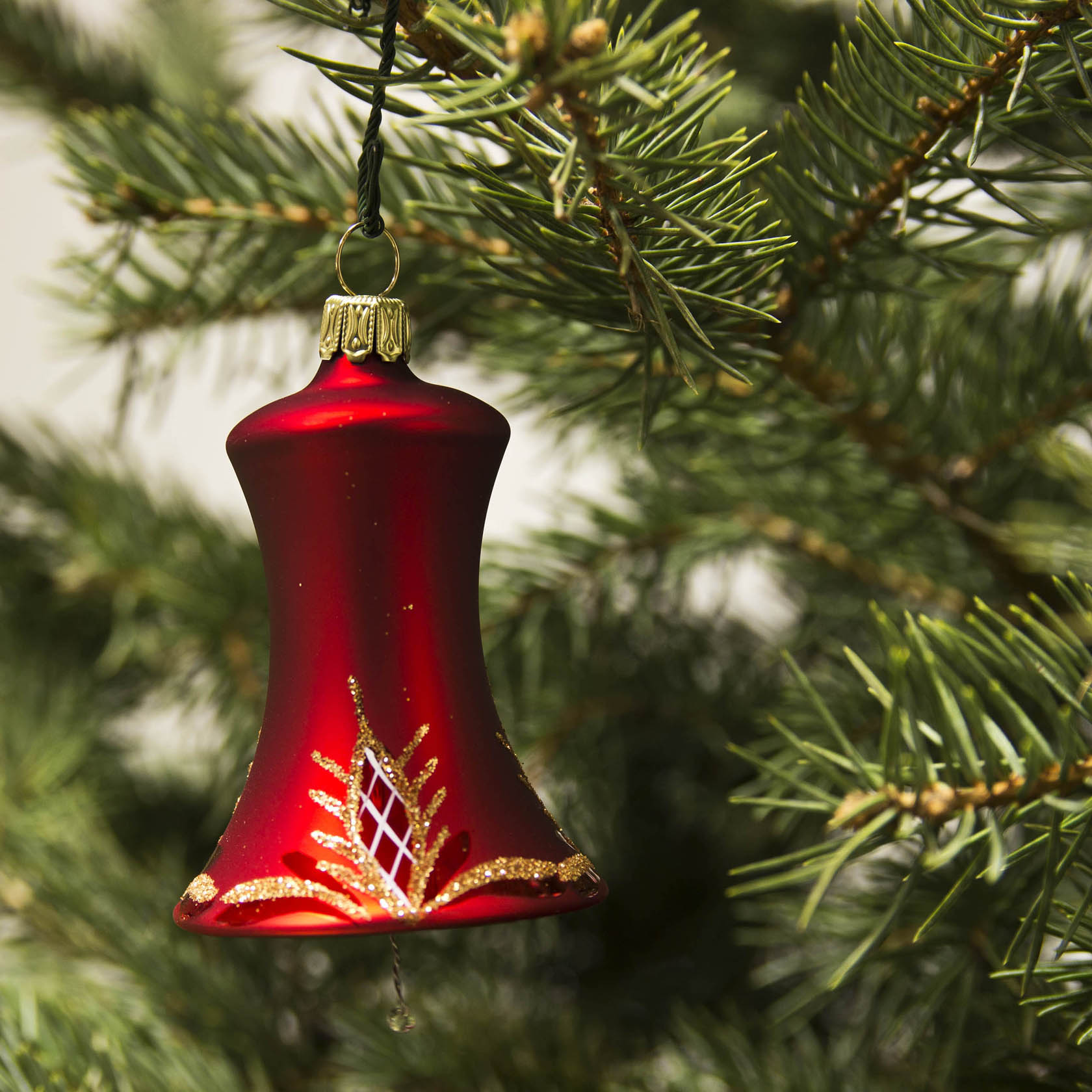 Eine rote, mattierte Glocke aus Glas mit Waffelmuster, hängt an einem Nadelzweig. Sie hat goldene Akzente und einen goldfarbenen Aufhänger.