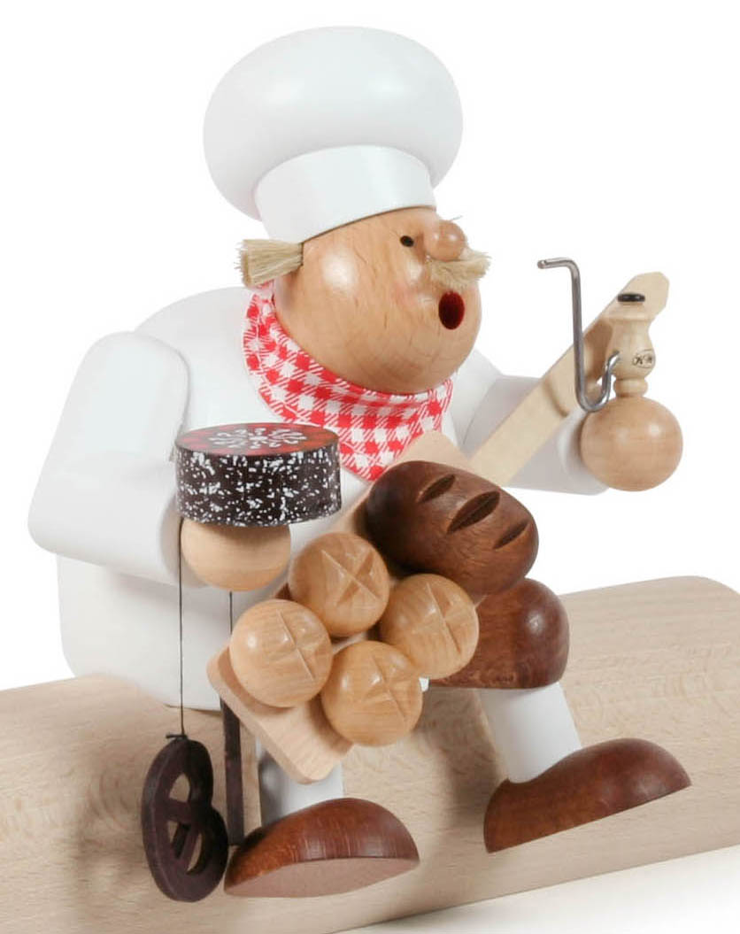 Holzfigur eines Rauchermanns in Bäckeroptik mit typischer Bäckermütze, rotem Halstuch, hält eine Brezel und einen Napfkuchen, sitzt auf Holzkante. im Dregeno Online Shop günstig kaufen