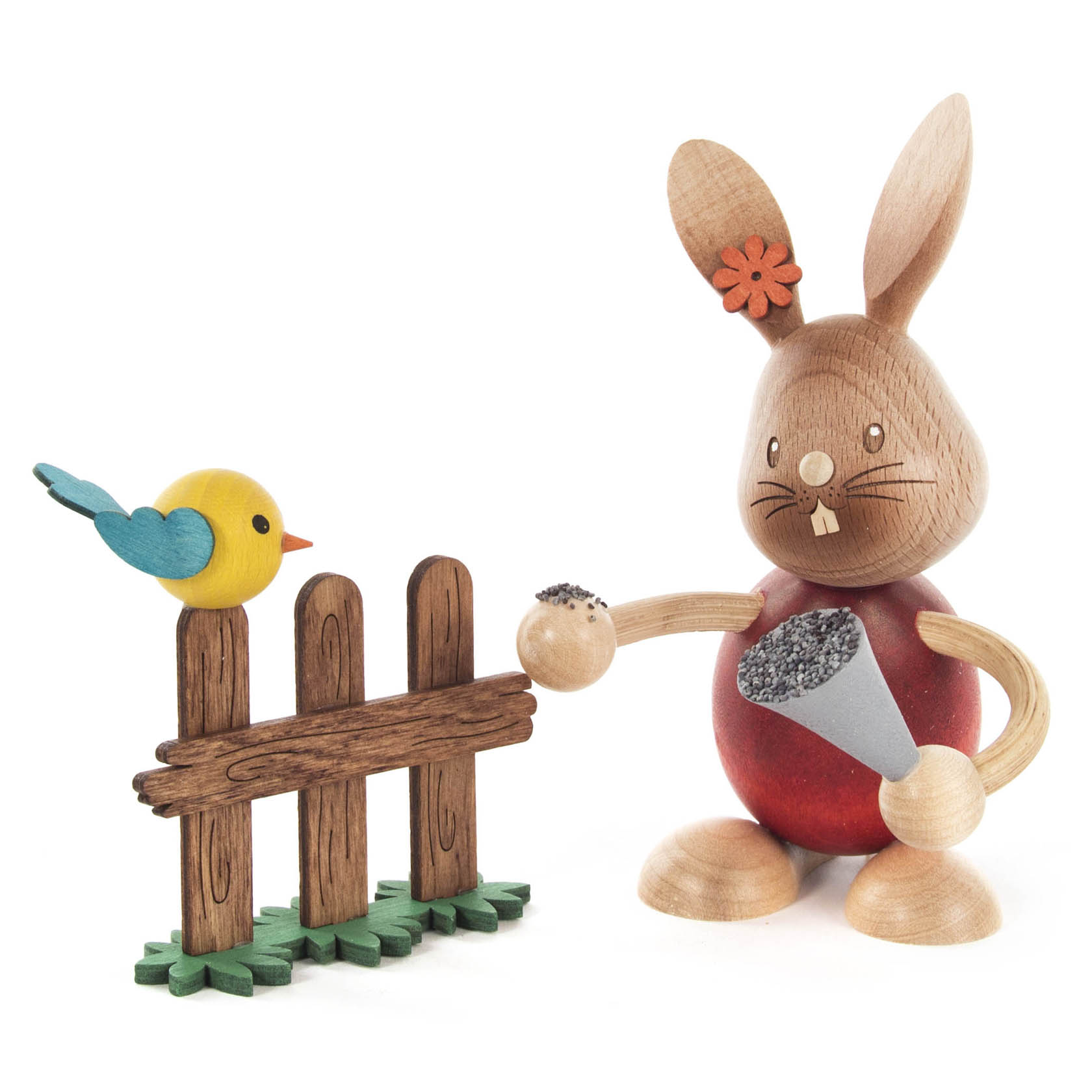 Holzhase Stupsi hält einen Kegel mit Samen, während ein gelber Vogel mit blauem Schwanz auf einem Holzzaun sitzt. im Dregeno Online Shop günstig kaufen