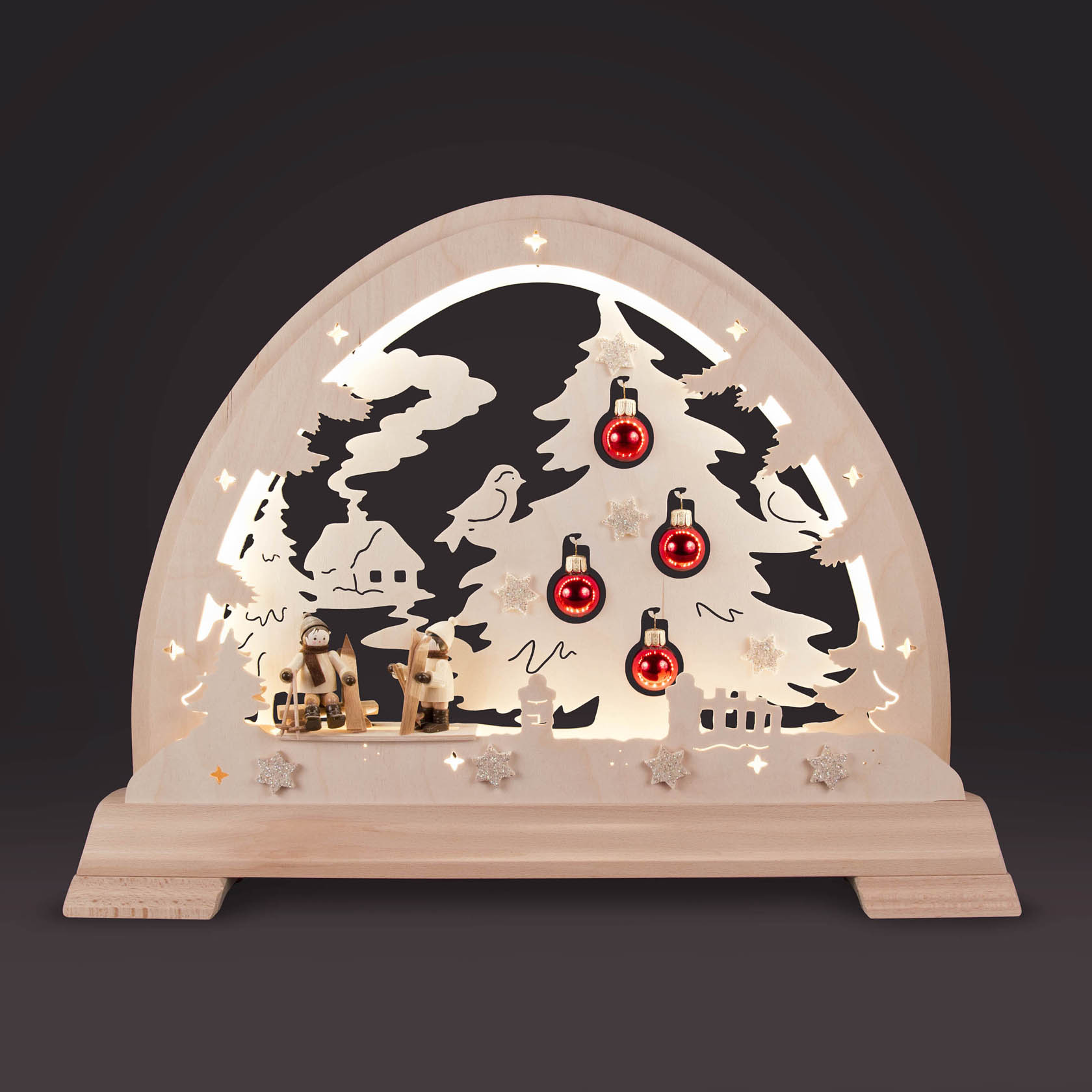 Ein beleuchteter Holz-Rundbogen mit Skifahrer-Figuren, einem Weihnachtsbaum mit roten Kugeln und LED-Band, Dekorationsschnee und Sterndetails.
