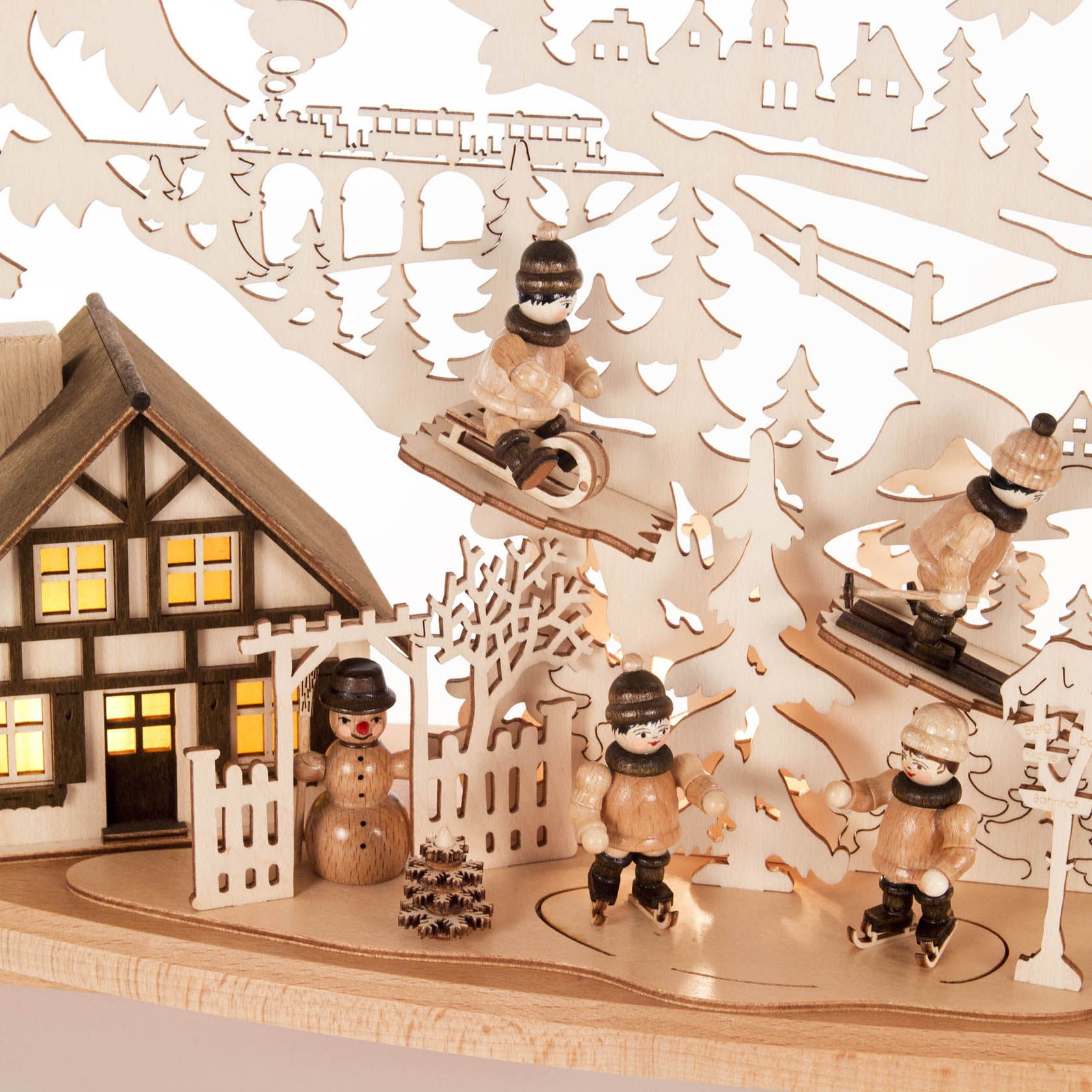 Ein beleuchteter Schwibbogen mit einem Fachwerkhaus, einem Schneemann und vier Holzfiguren beim Wintersport: zwei auf Skiern, eine mit einem Schlitten.