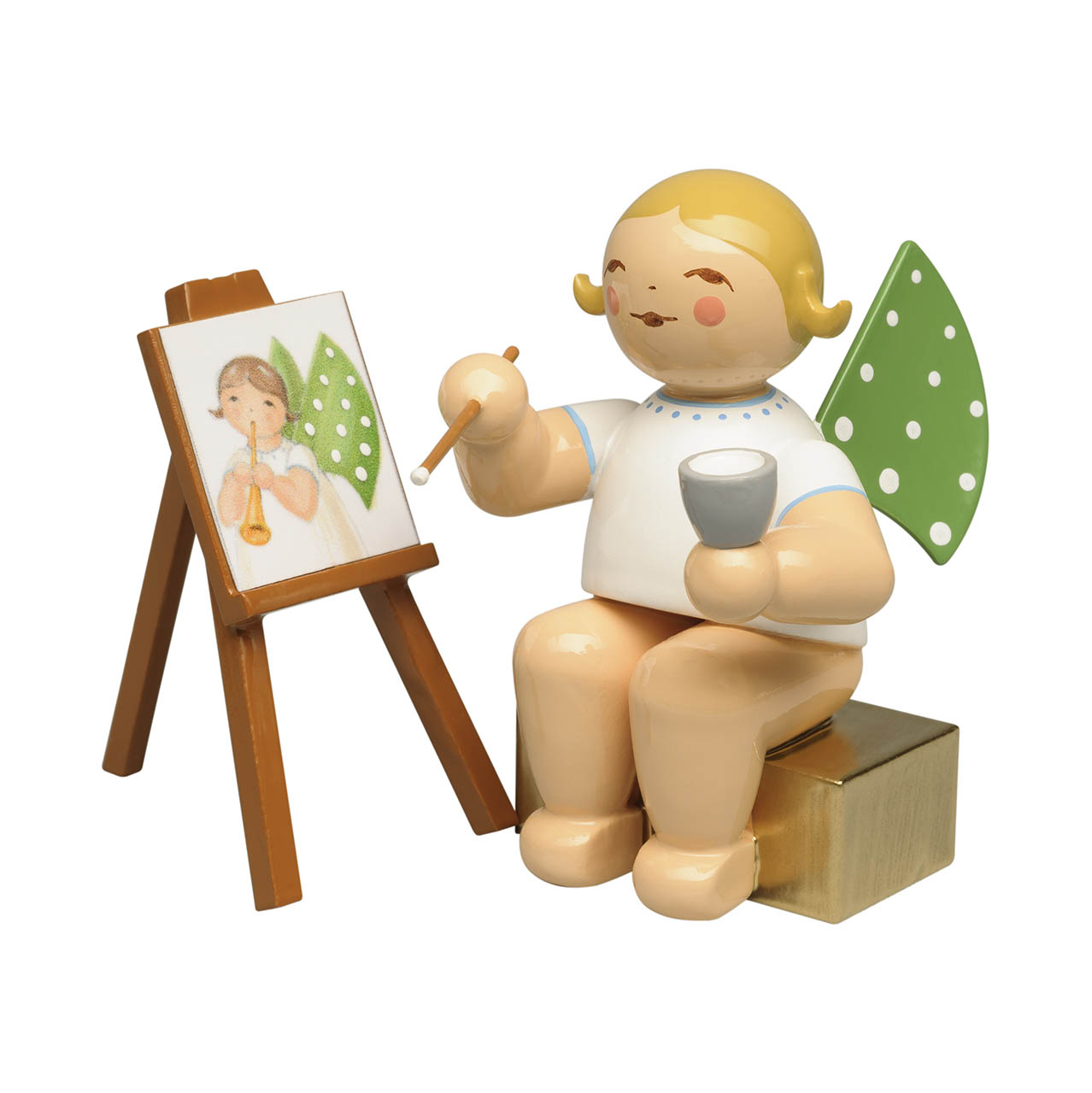 Ein Engel aus Holz sitzt auf einem goldenem Würfel und malt mit einem Pinsel auf einer Staffelei ein Bild eines Engels mit grünen Flügeln. im Dregeno Online Shop günstig kaufen