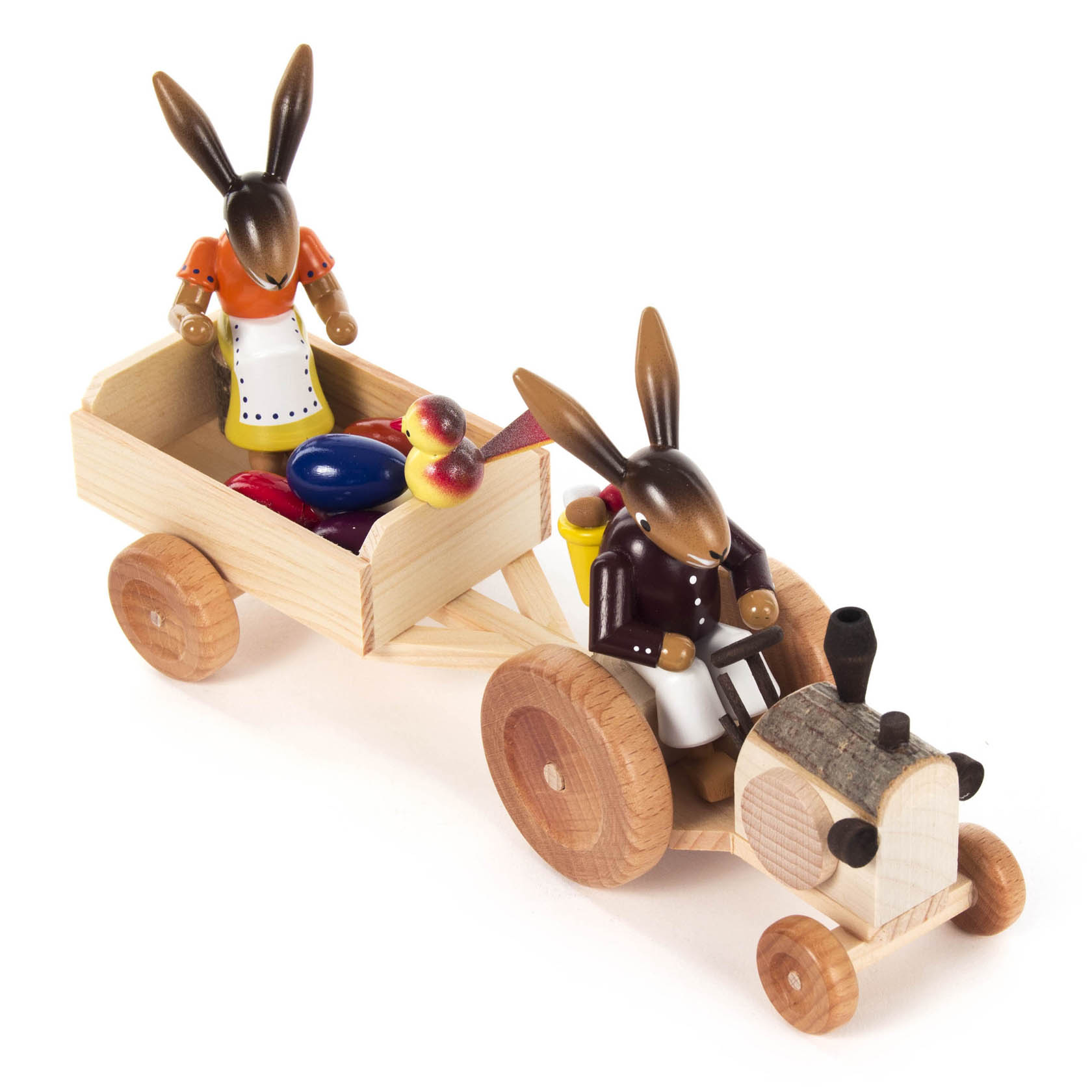 Holzfiguren eines Hasenpaares auf einem handgefertigten, hölzernen Traktor mit Anhänger. Der hintere Hase hält bunte Ostereier im Anhänger.
