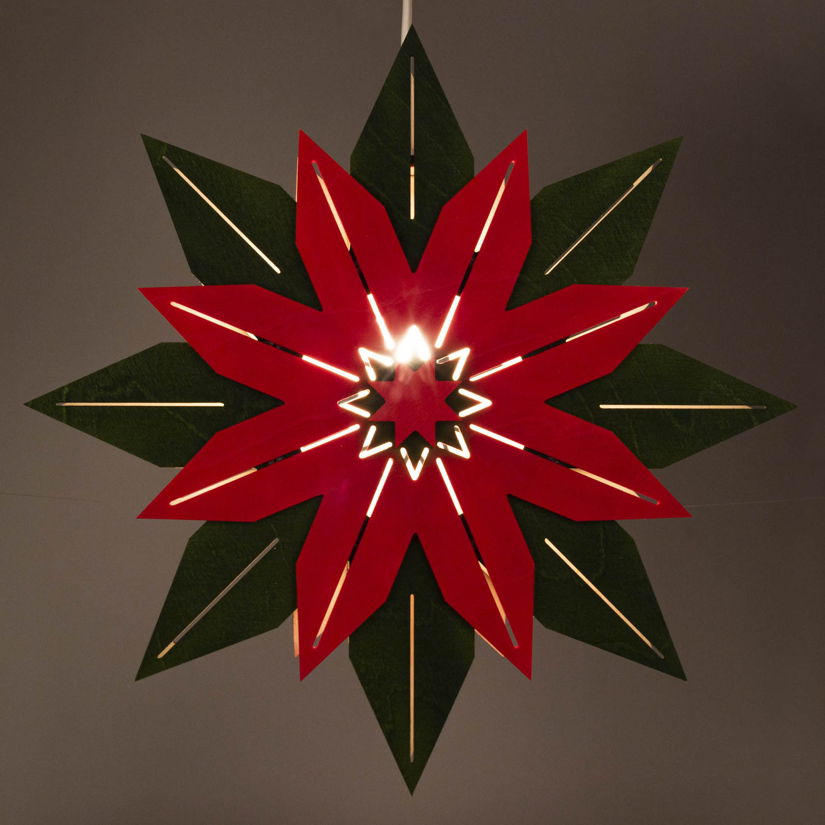 Ein grüner und roter Weihnachtsstern aus Papier mit elektrischer Beleuchtung, die durch die roten und grünen Blätter scheint.