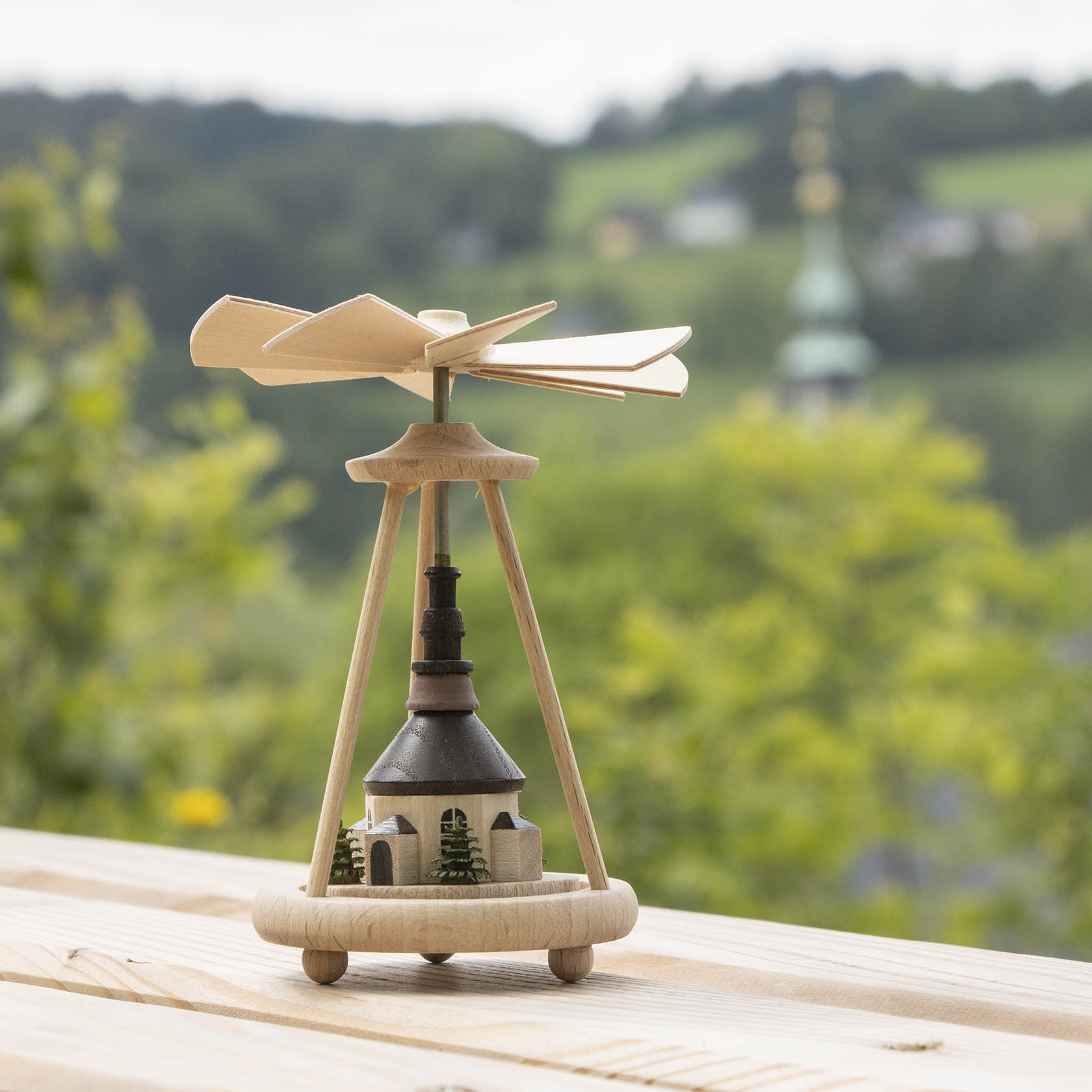 Ein Wärmespiel mit der Miniatur der Seiffener Kirche, das auf einem Holztisch steht. Oben dreht sich ein Propeller aus Holz.