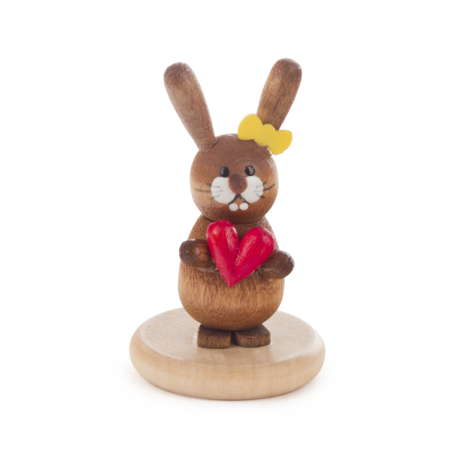 Ein hölzerner Hase mit gelber Schleife hält ein rotes Herz auf einem runden Sockel.