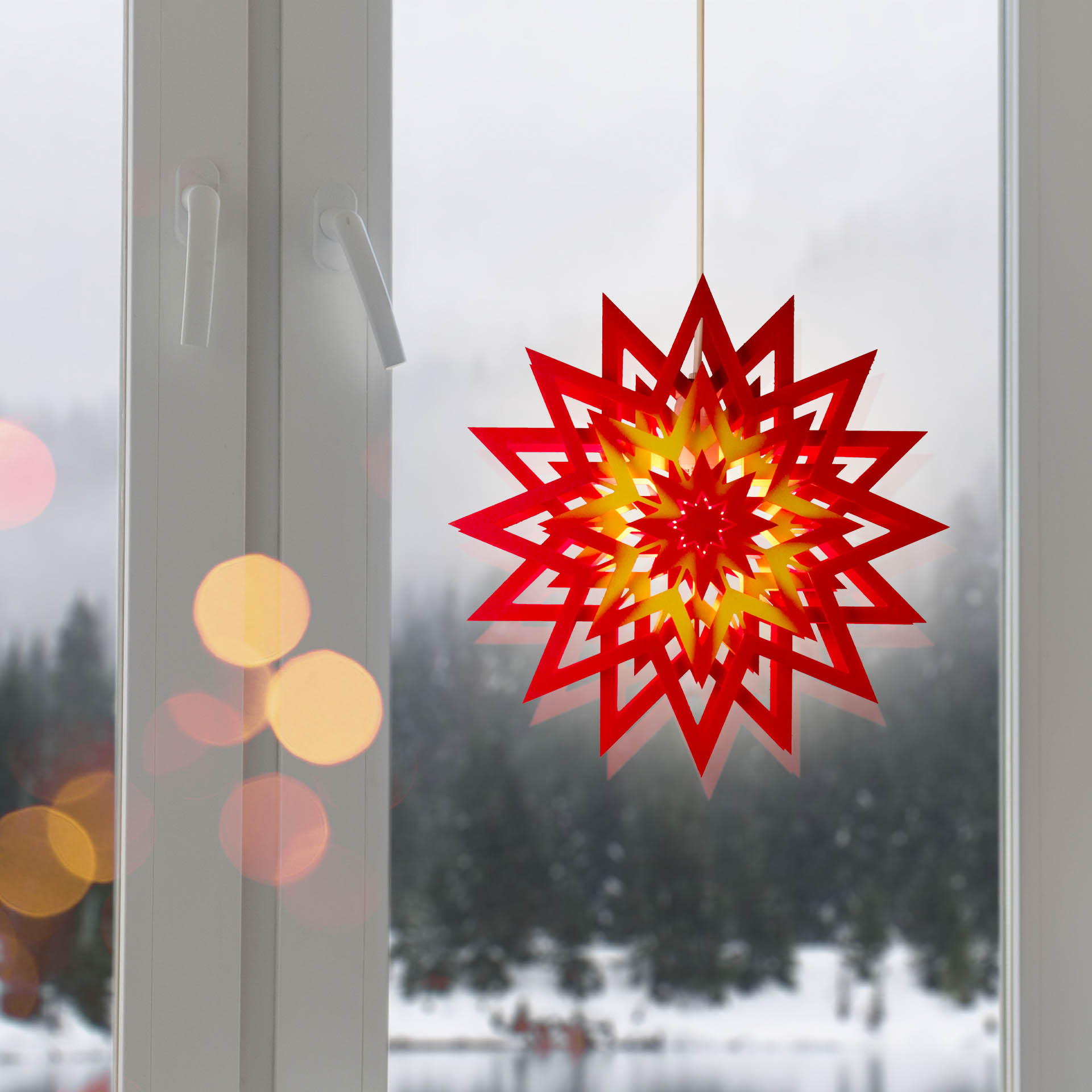 Ein roter, neunspitziger Weihnachtsstern aus Papier mit gelber Beleuchtung hängt vor einem Fenster.