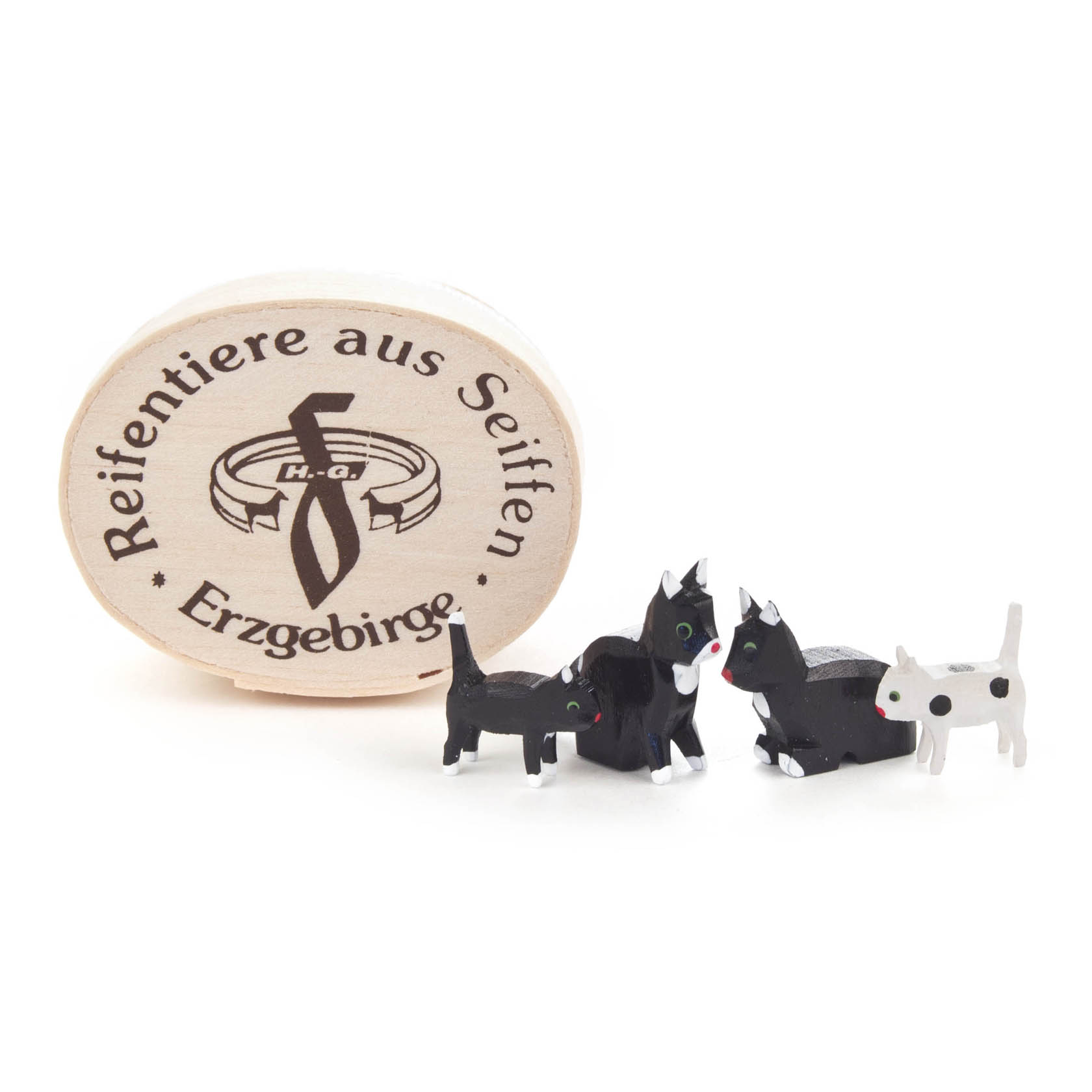 Drei kleine, handgeschnitzte Katzenfiguren aus Holz, schwarz-weiß bemalt, stehen vor einer ovalen Holzspandose mit der Aufschrift 'Reifentiere aus Seiffen, Erzgebirge'. im Dregeno Online Shop günstig kaufen