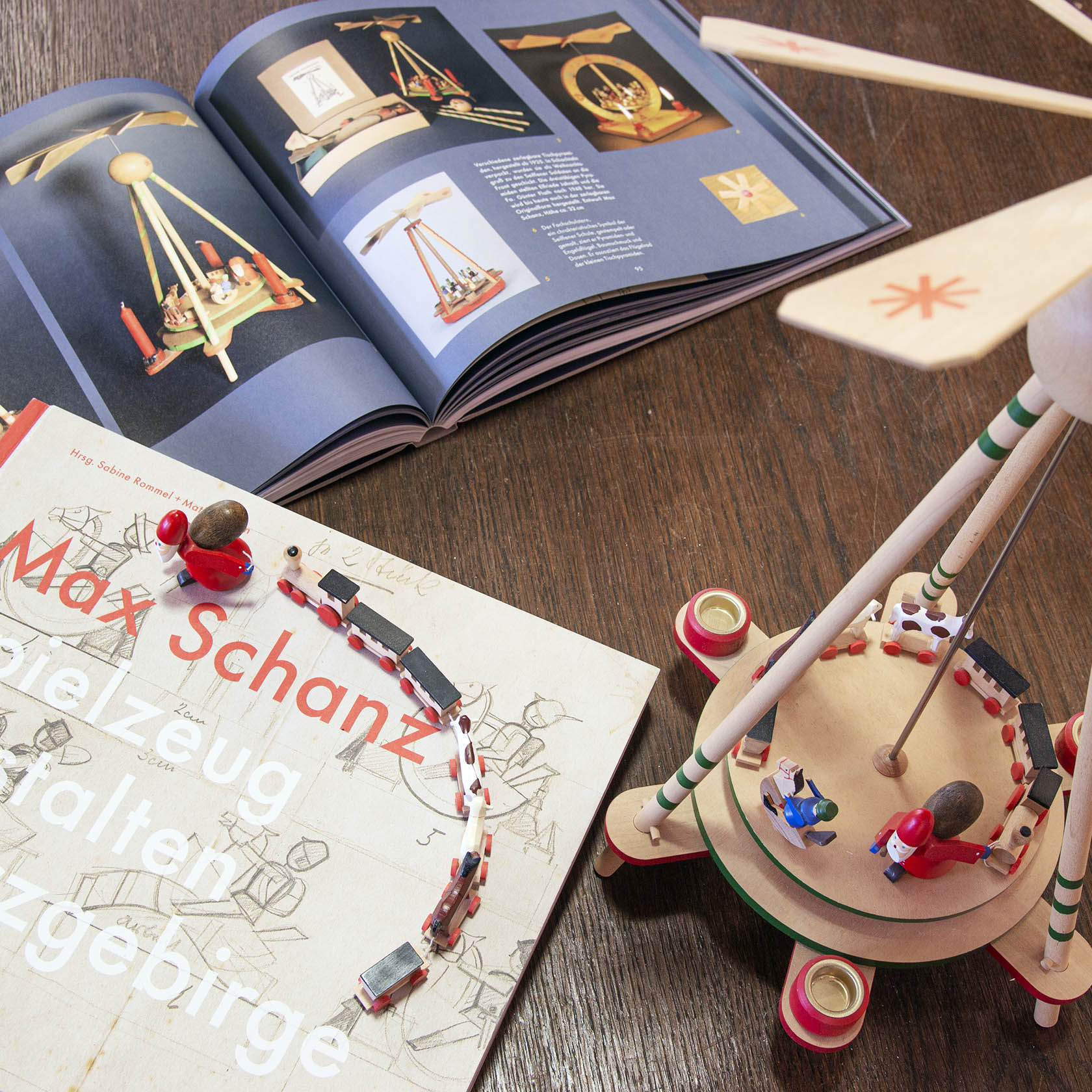 Stabpyramide mit einem Weihnachtsmann und Spielzeugfiguren. Auf einem Tisch steht ein aufgeschlagenes Buch mit ähnlichen Pyramidenabbildungen.