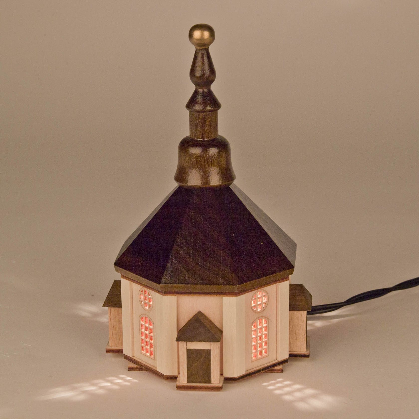 Ein kleines Lichterhaus in Form der Seiffener Kirche mit beleuchteten Fenstern und dunklem Holz-Dach und Turm.