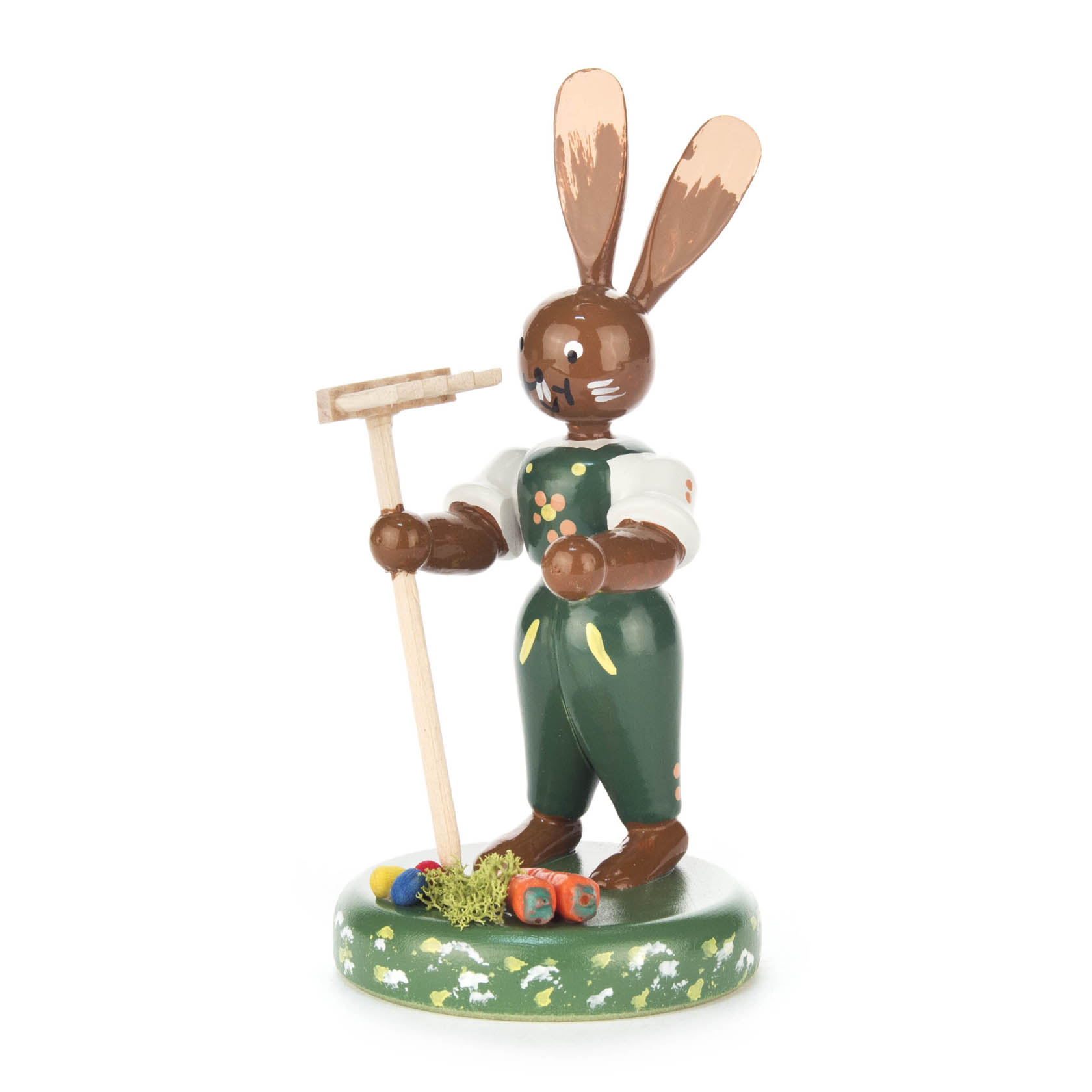 Holzfigur: Hase mit bemaltem Gesicht in grüner Latzhose, hält einen Rechen; steht auf grünem Sockel mit bemalten Blumen und Eiern. im Dregeno Online Shop günstig kaufen