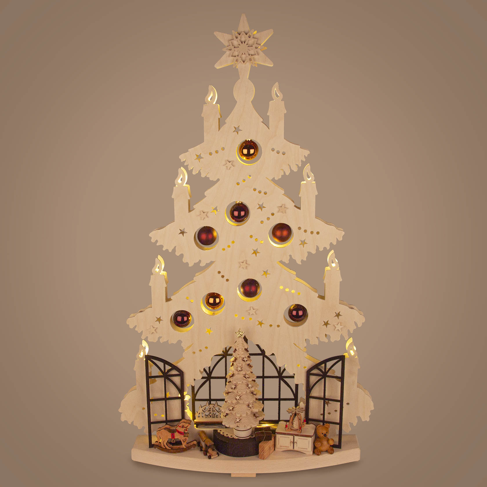 Ein Schwibbogen in Form einer Tanne, verziert mit Kerzen und roten Kugeln, zeigt unten eine Weihnachtsstube mit Fenstern, einem Baum und Spielzeug.