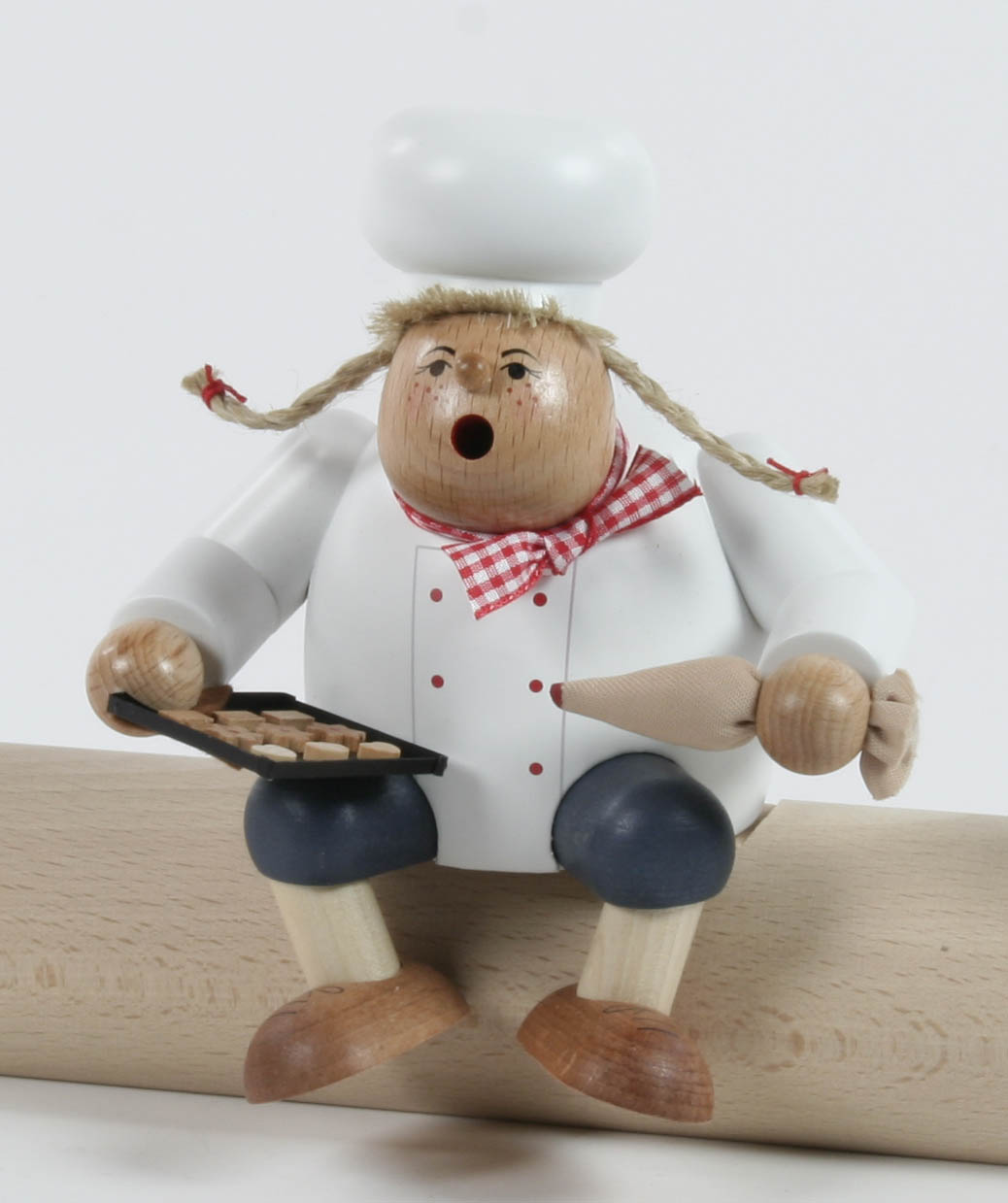 Holzfigur einer Konditorin mit weißem Kochhut und kariertem Halstuch, die auf einem Brett sitzt. Sie hält ein Backblech und einen Spritzbeutel. im Dregeno Online Shop günstig kaufen