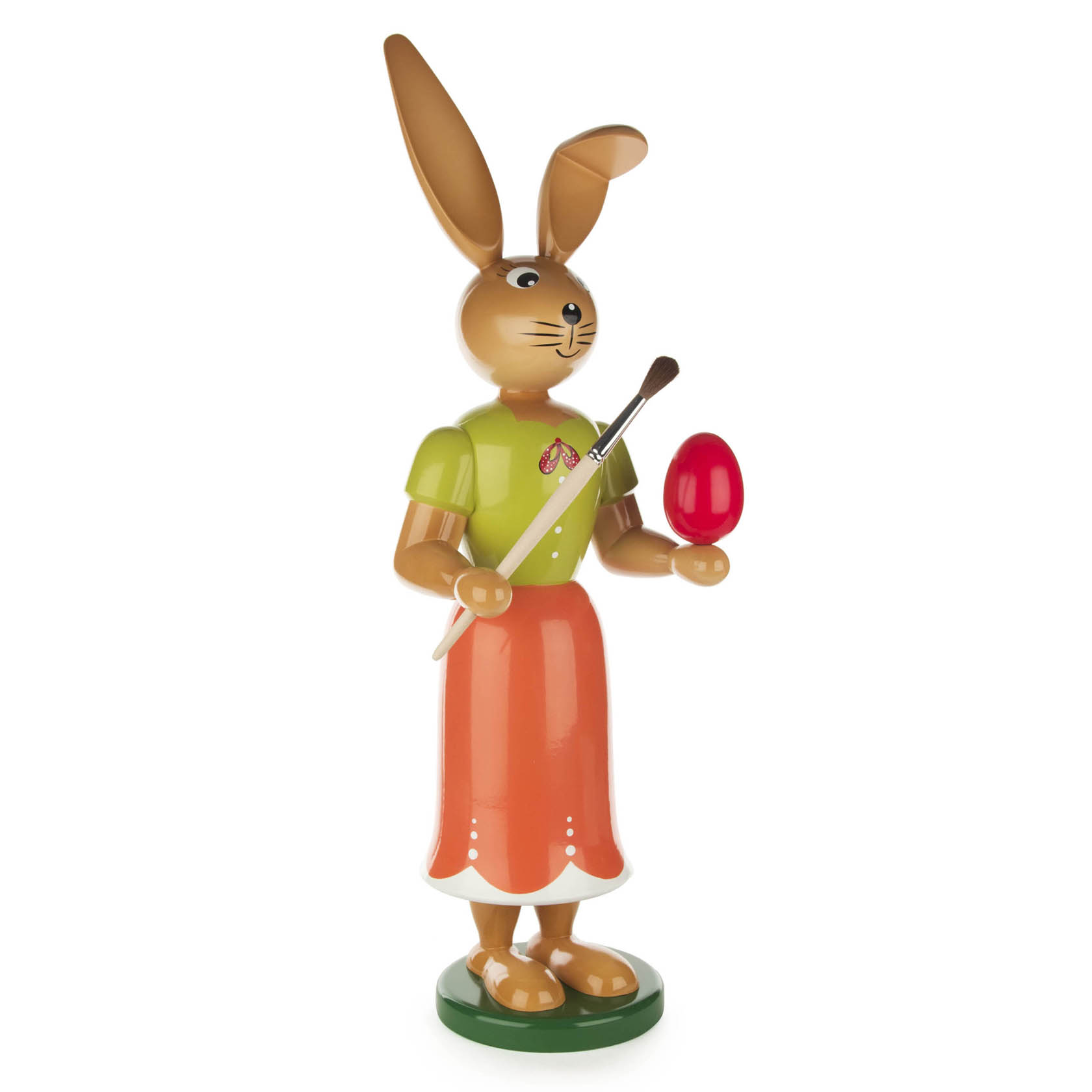 Eine handgefertigte Holzfigur einer Hasenmalerin, die ein rotes Osterei und einen Pinsel hält. Sie trägt ein grünes Oberteil und einen orangenen Rock. im Dregeno Online Shop günstig kaufen