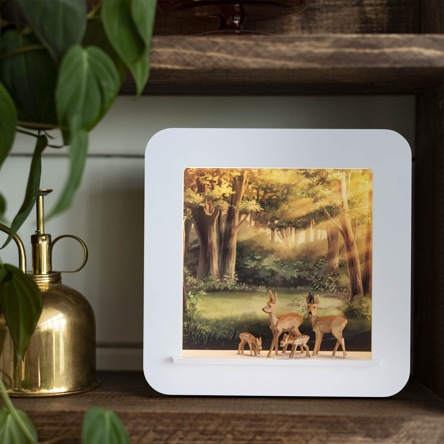 Ein dekorativer Objektrahmen mit einer LED-Beleuchtung, die drei Rehe in einem Waldmotiv beleuchtet. Die Rehe stehen vor einem Hintergrund aus Bäumen und sonnigem Himmel.
