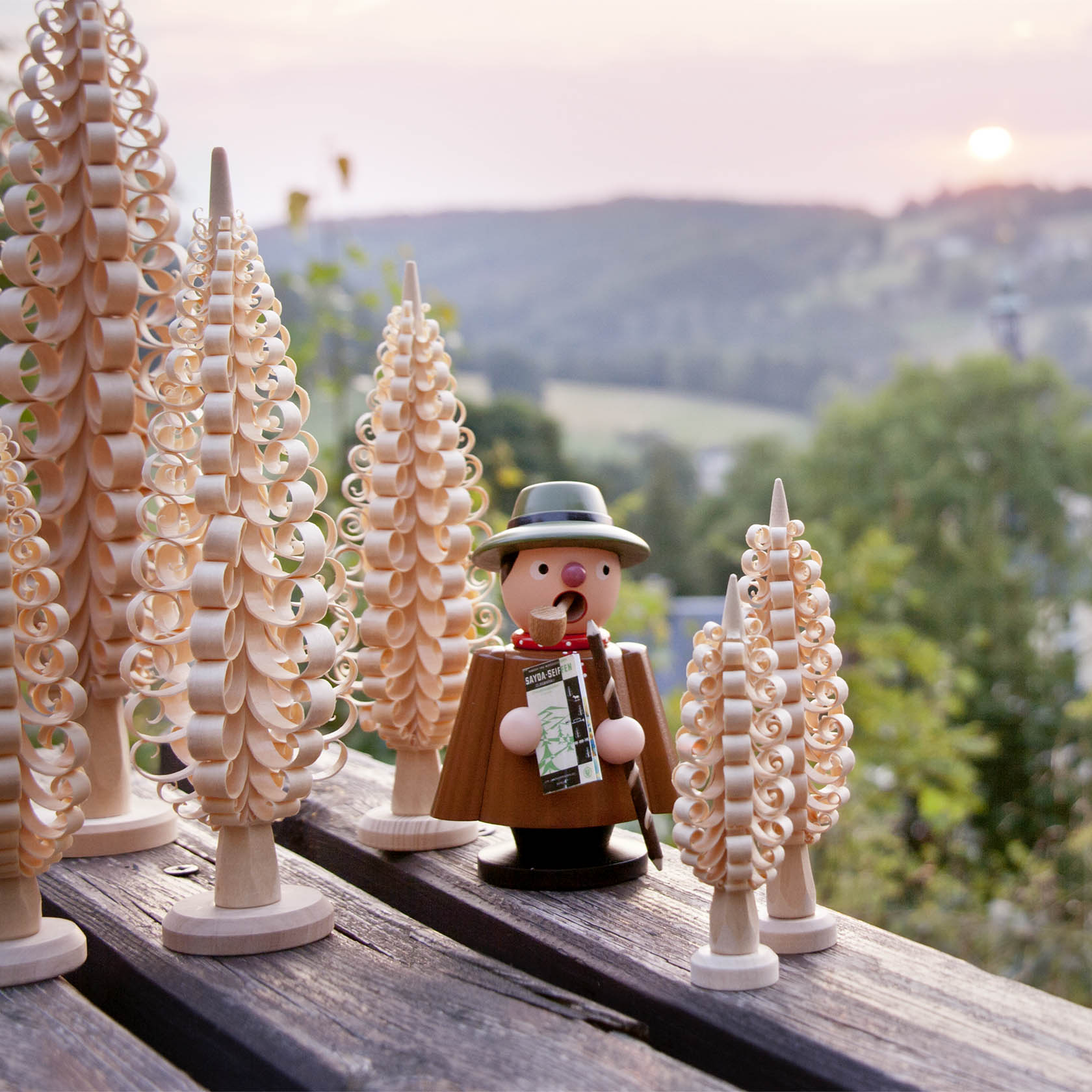 Ein traditioneller deutscher Räuchermann in Form eines Wanderers steht auf einem Holztisch, umgeben von geschnitzten Holzbäumen.