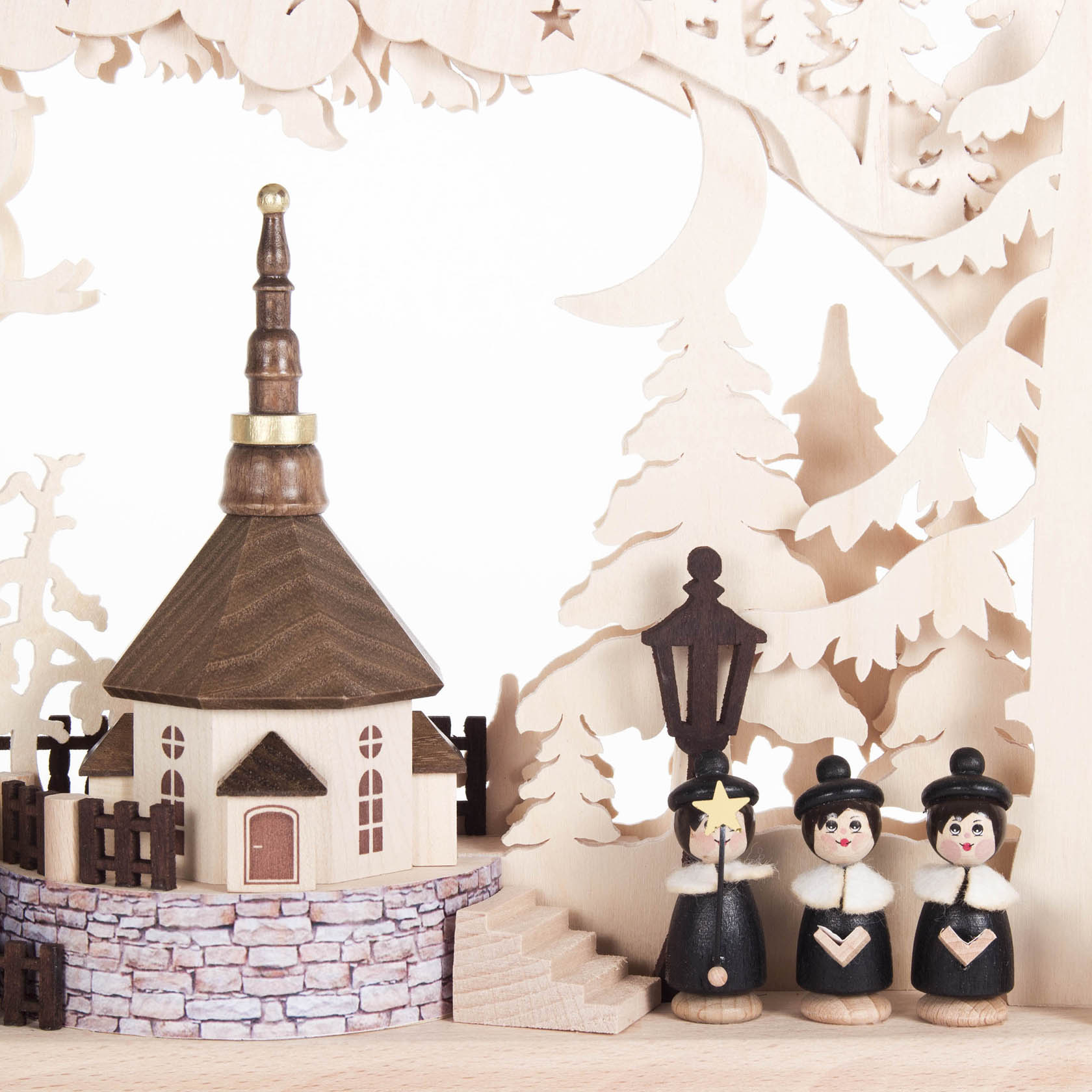 A small wooden arch candle holder depicting a village church, indirectly illuminated. It features three wooden figures dressed in black choir attire.