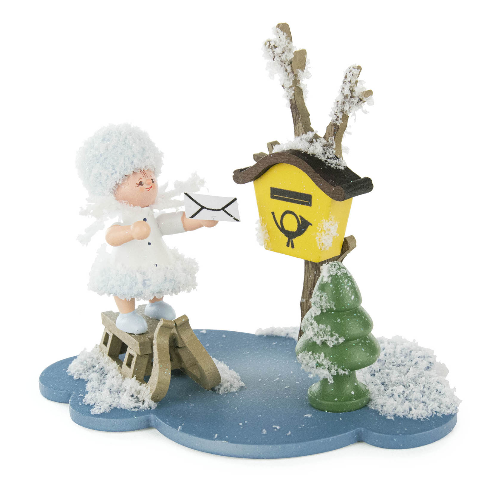 Holzfigur eines Schneeflöckchens in weißem Kleid und Mütze, das einen Brief in einen gelben Briefkasten mit Schnee einwirft, daneben ein schneebedeckter Baum. im Dregeno Online Shop günstig kaufen
