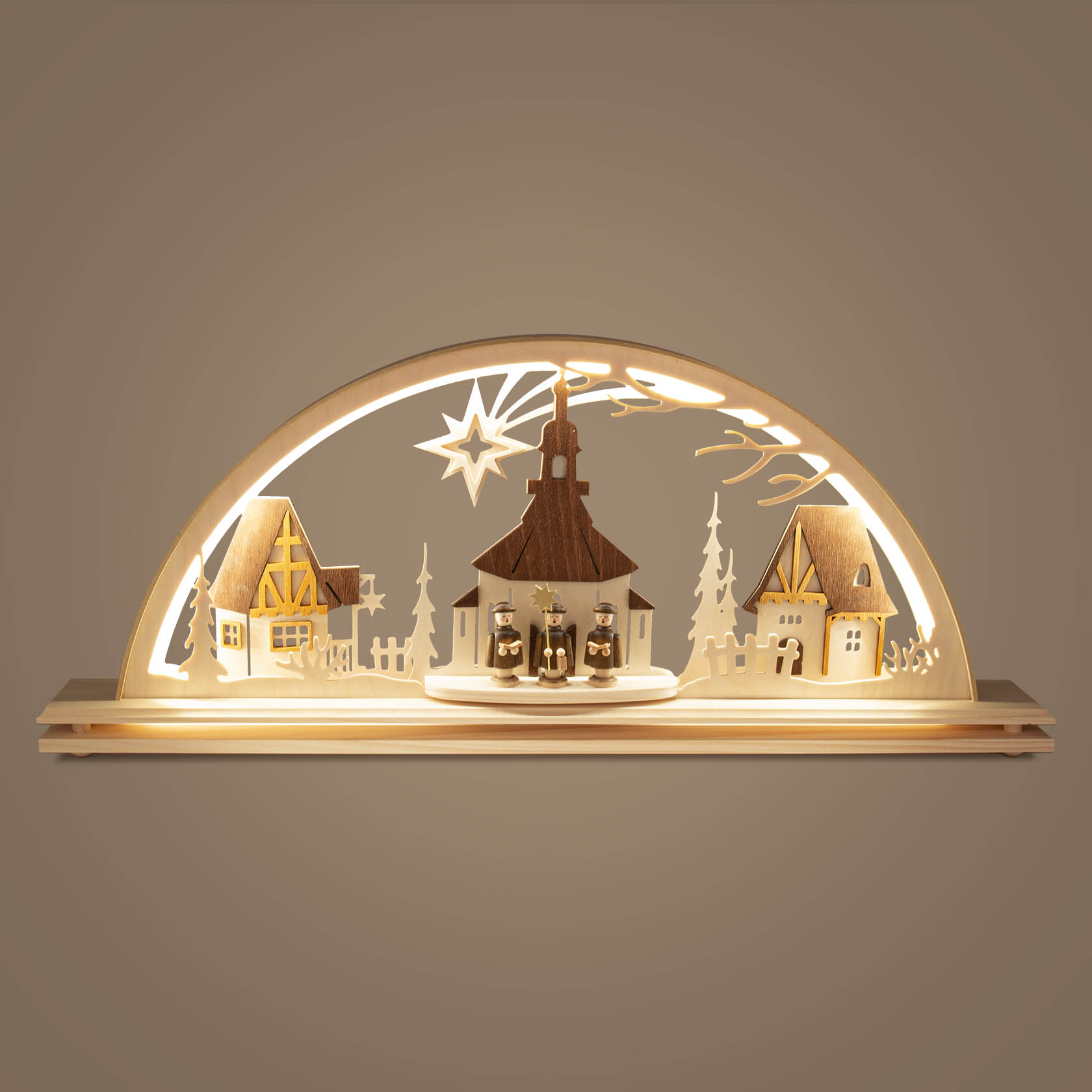 Ein beleuchteter Schwibbogen zeigt die Seiffener Kirche in der Mitte, flankiert von zwei Häusern, alles in einem hellen Holz gefertigt.