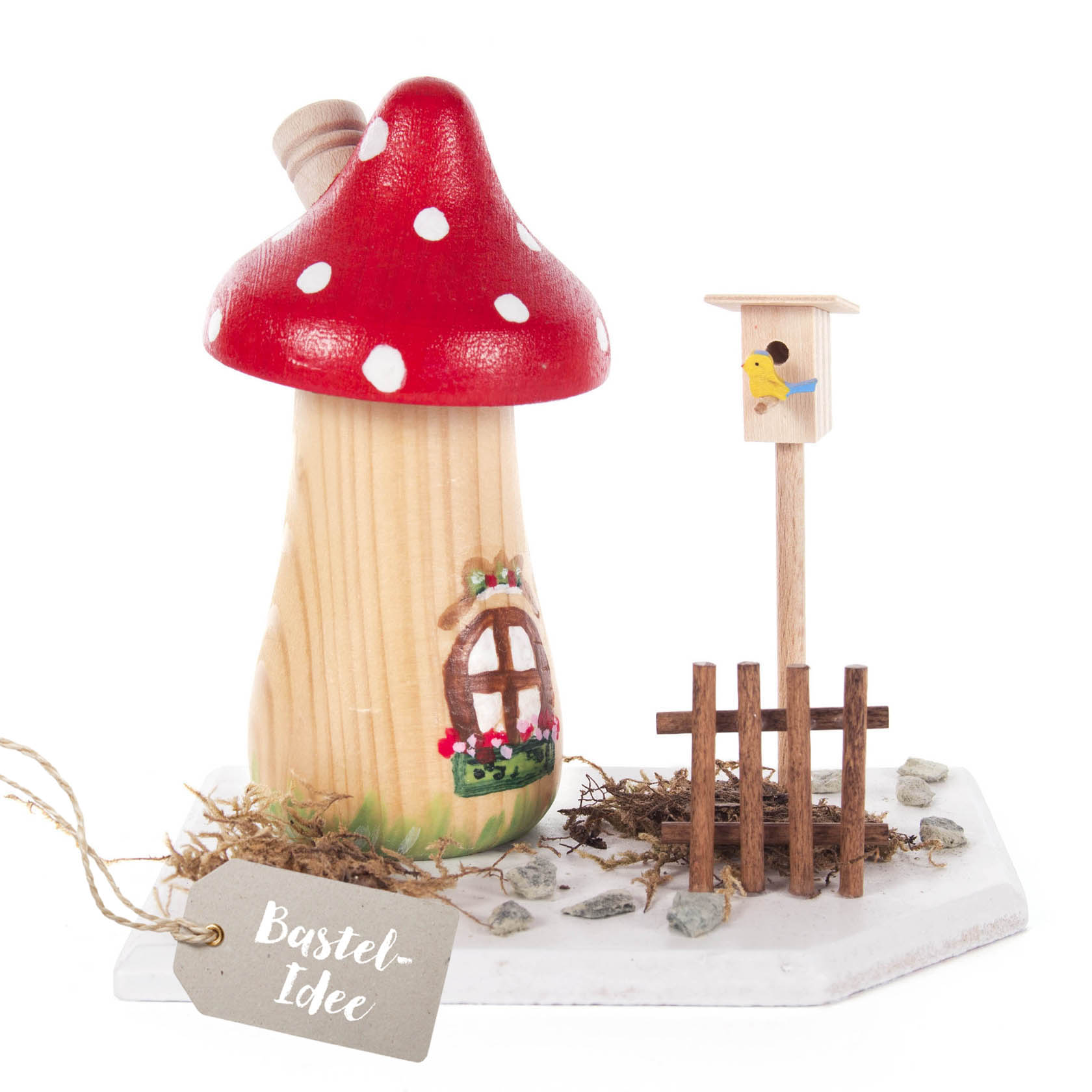 Ein Bastelset bestehend aus einem hölzernen Räucherpilz mit rotem Hut und weißen Punkten, einem Vogelhäuschen und kleinem Zaun auf einer weißen Platte. im Dregeno Online Shop günstig kaufen