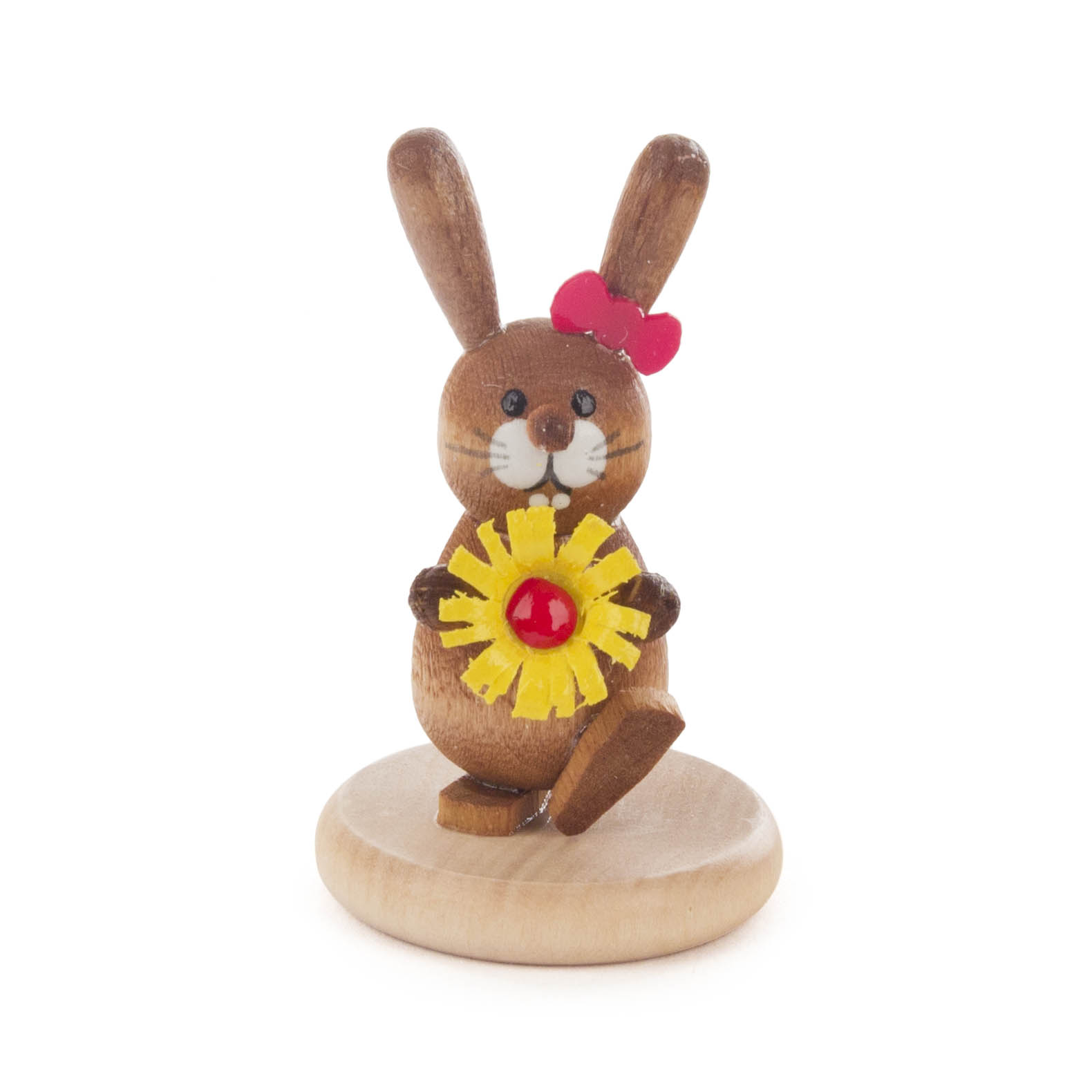 Eine farbig lasierte Holzfigur eines sitzenden Hasen mit einer roten Schleife und einer gelben Blume auf einem runden Sockel.