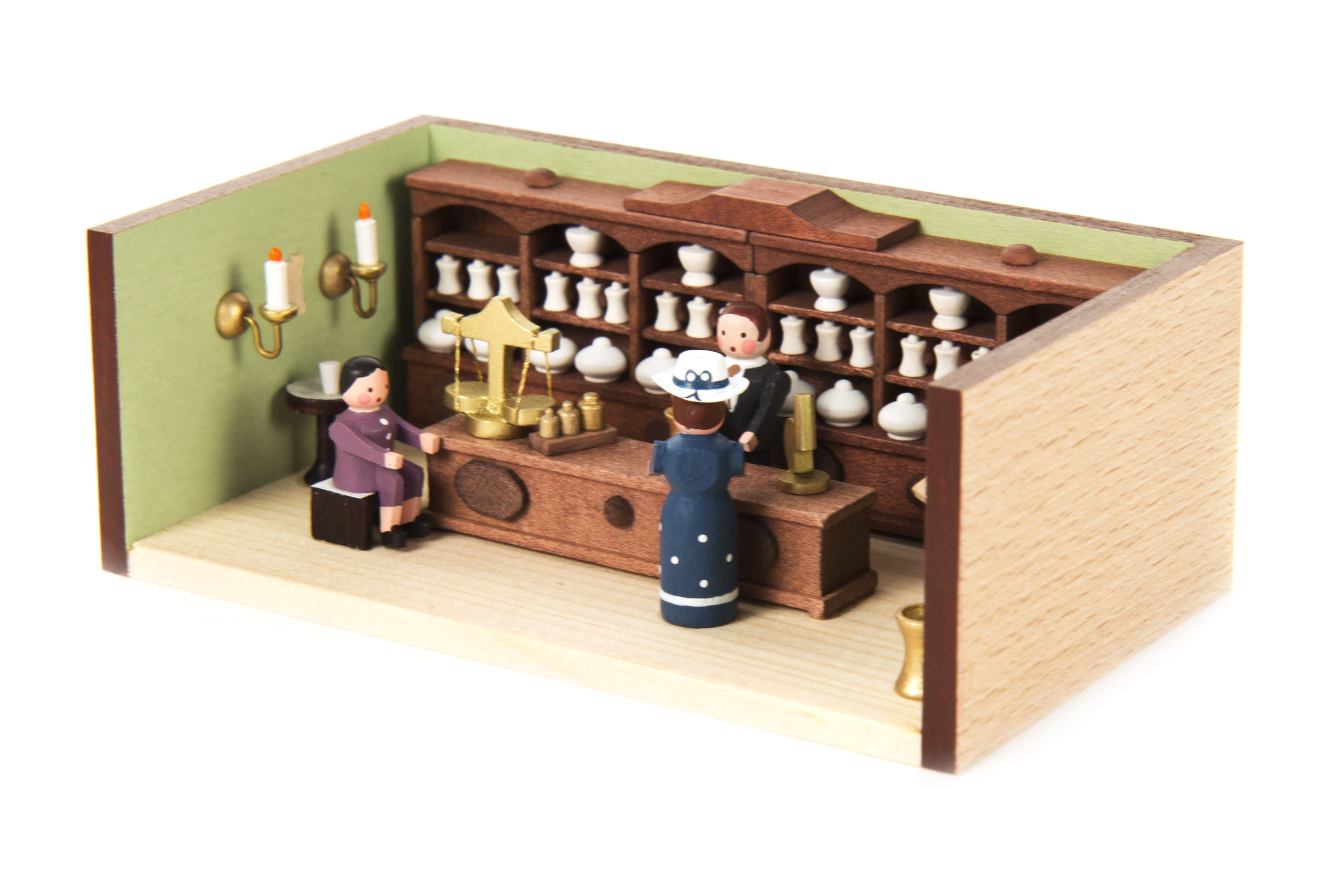 Miniaturmodell einer Apotheke mit einem Apotheker hinter dem Tresen und zwei Kunden, die beraten werden. Regale mit Krügen und eine Waage sind sichtbar.