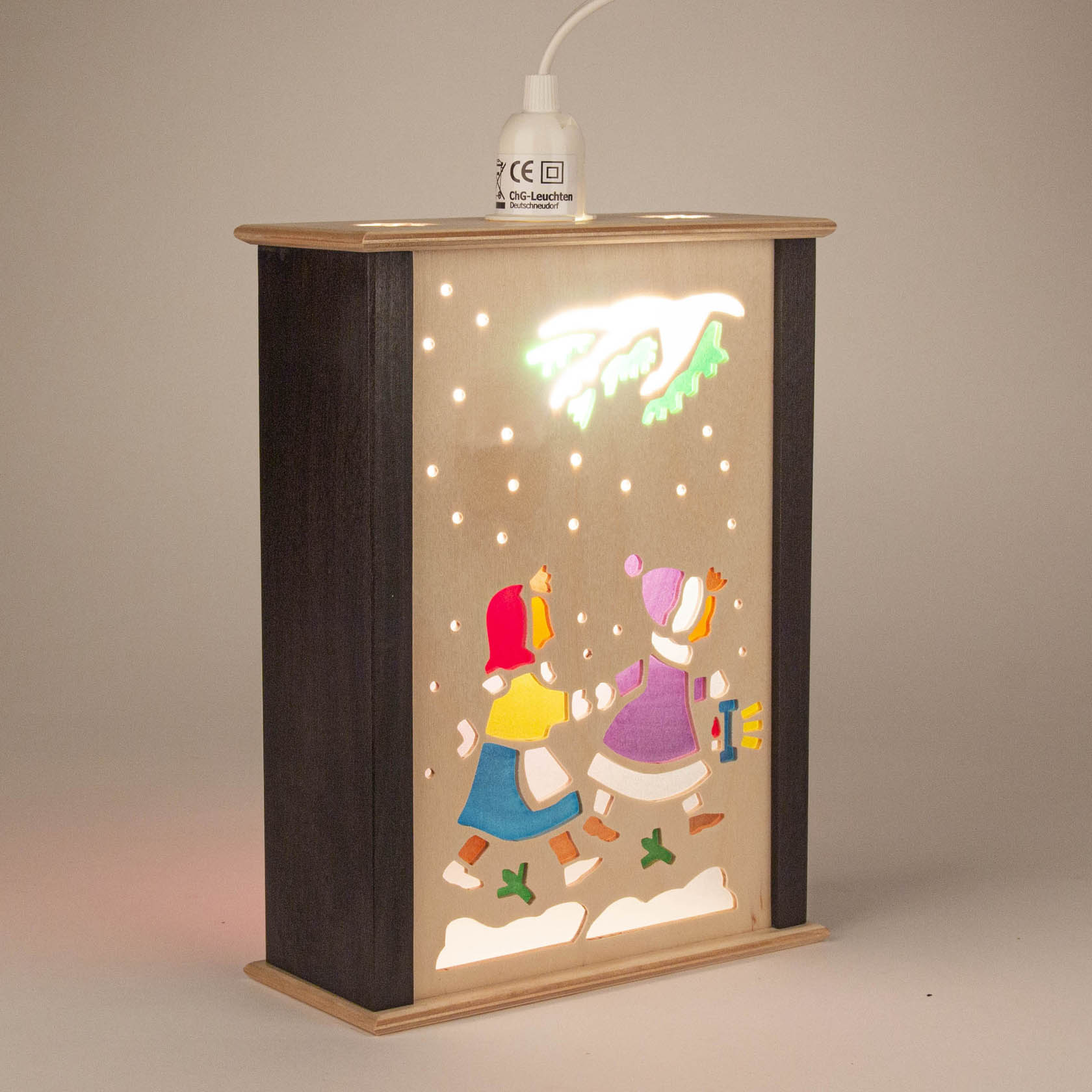 Kleine Fensterlaterne mit zwei Kindern in Winterkleidung, die durch den Schnee gehen. Eines der Kinder trägt ein Geschenk.