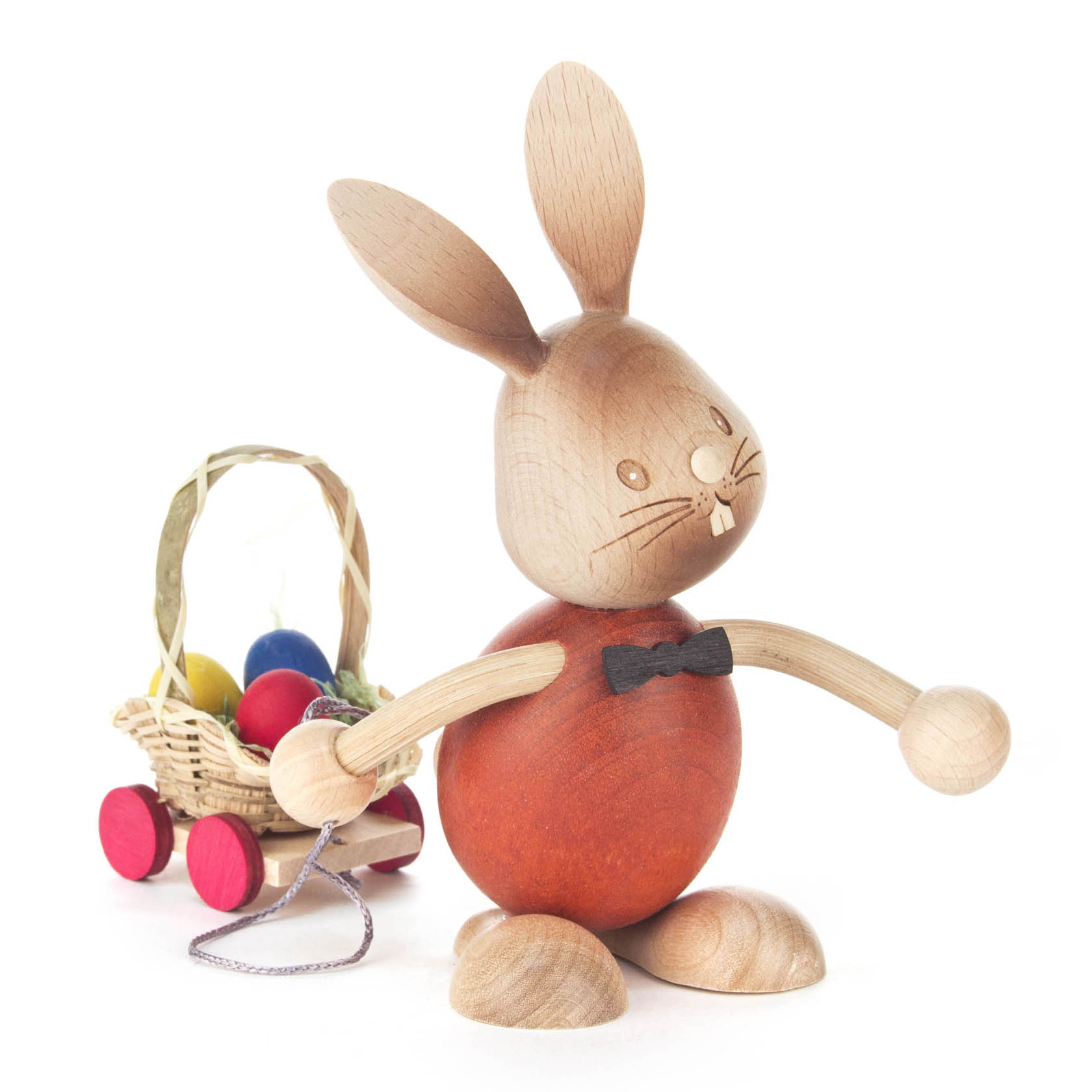 Eine Holzfigur in Form eines Hasen namens 'Stupsi', der einen Eierwagen mit bunten Ostereiern zieht. Der Hase trägt eine schwarze Fliege. im Dregeno Online Shop günstig kaufen