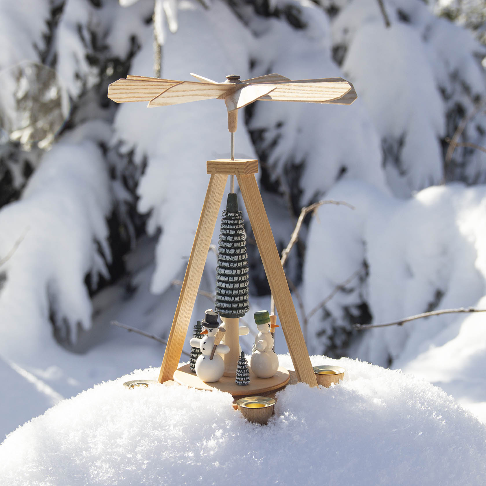 Holzpyramide mit Schneemännern und Kerzenhaltern, steht auf einer schneebedeckten Oberfläche.