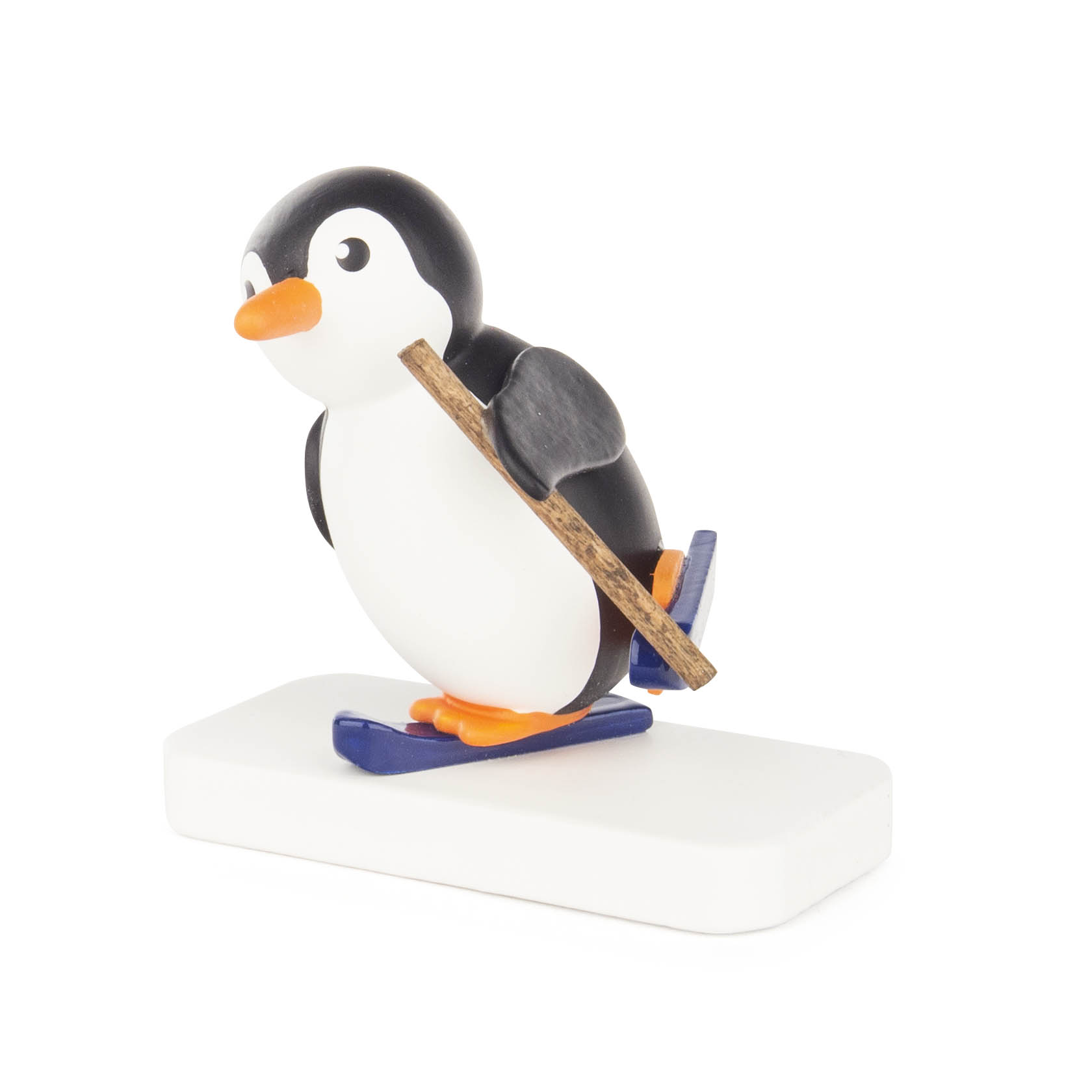 Eine Figur eines Pinguins in Anfängerpose mit Skiern und Skistock auf einem weißen Sockel.