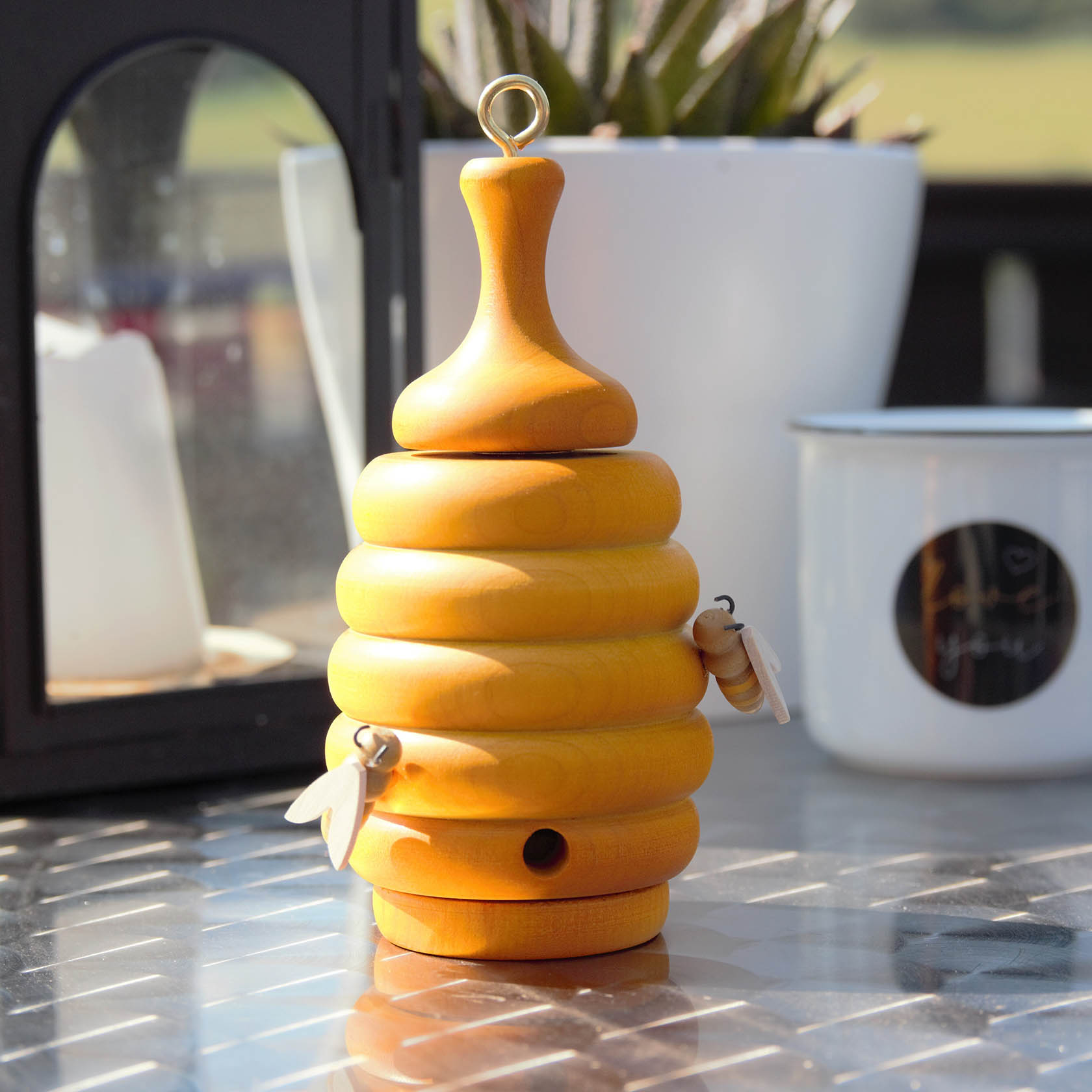 Holzbienenstock in Form eines Räucherofens, mit abgerundeter Spitze und zwei hölzernen Bienen, auf einem Tisch stehend.