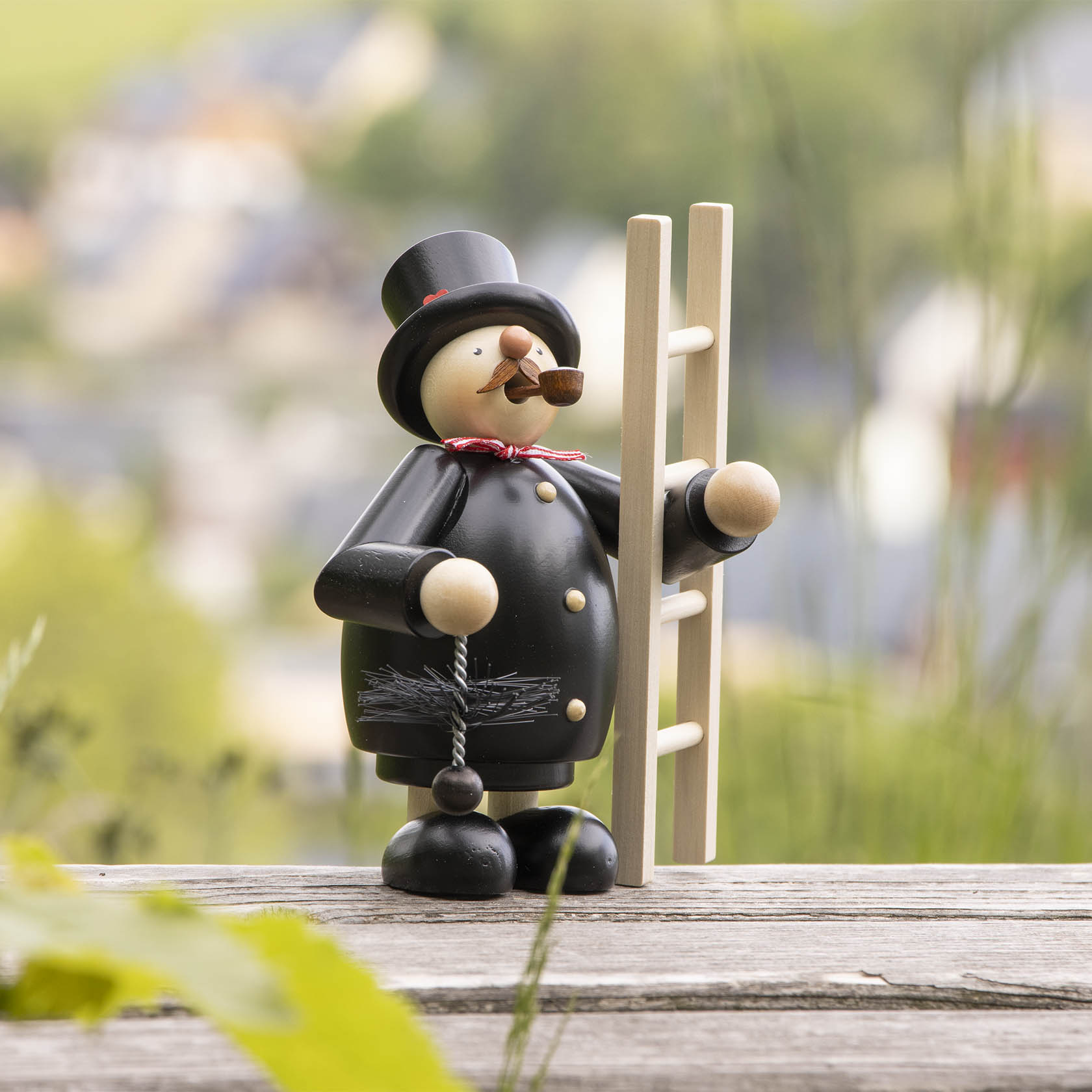 Ein Räuchermann in Form eines Schornsteinfegers, der eine Leiter hält und eine Pfeife raucht. Er trägt einen schwarzen Anzug mit Zylinder und hat rote Fliege.