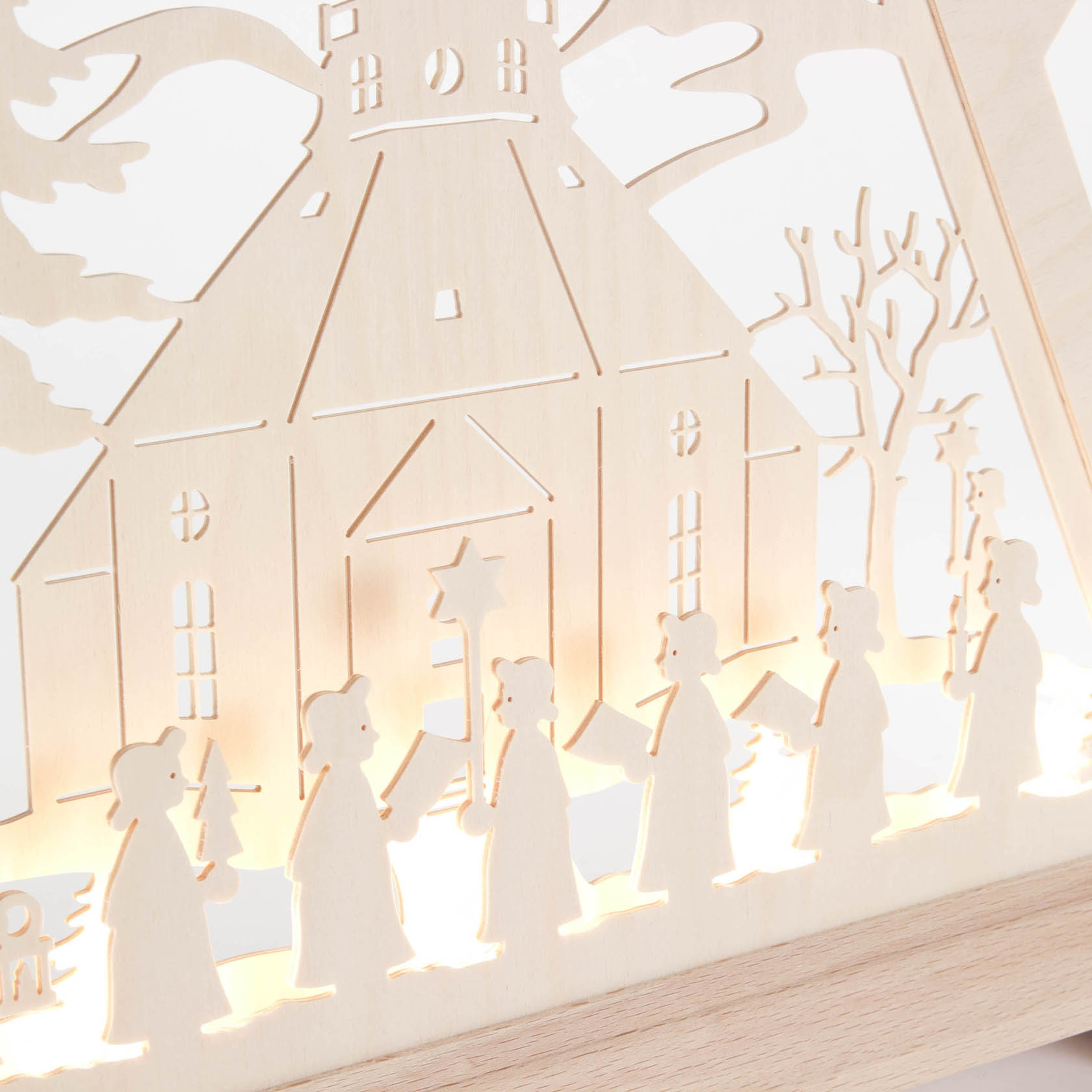 Ein Weihnachtsdreieck aus Holz zeigt die Seiffener Kirche. Davor stehen mehrere Kurrende-Sänger mit Notenblättern und beleuchten das Bild.