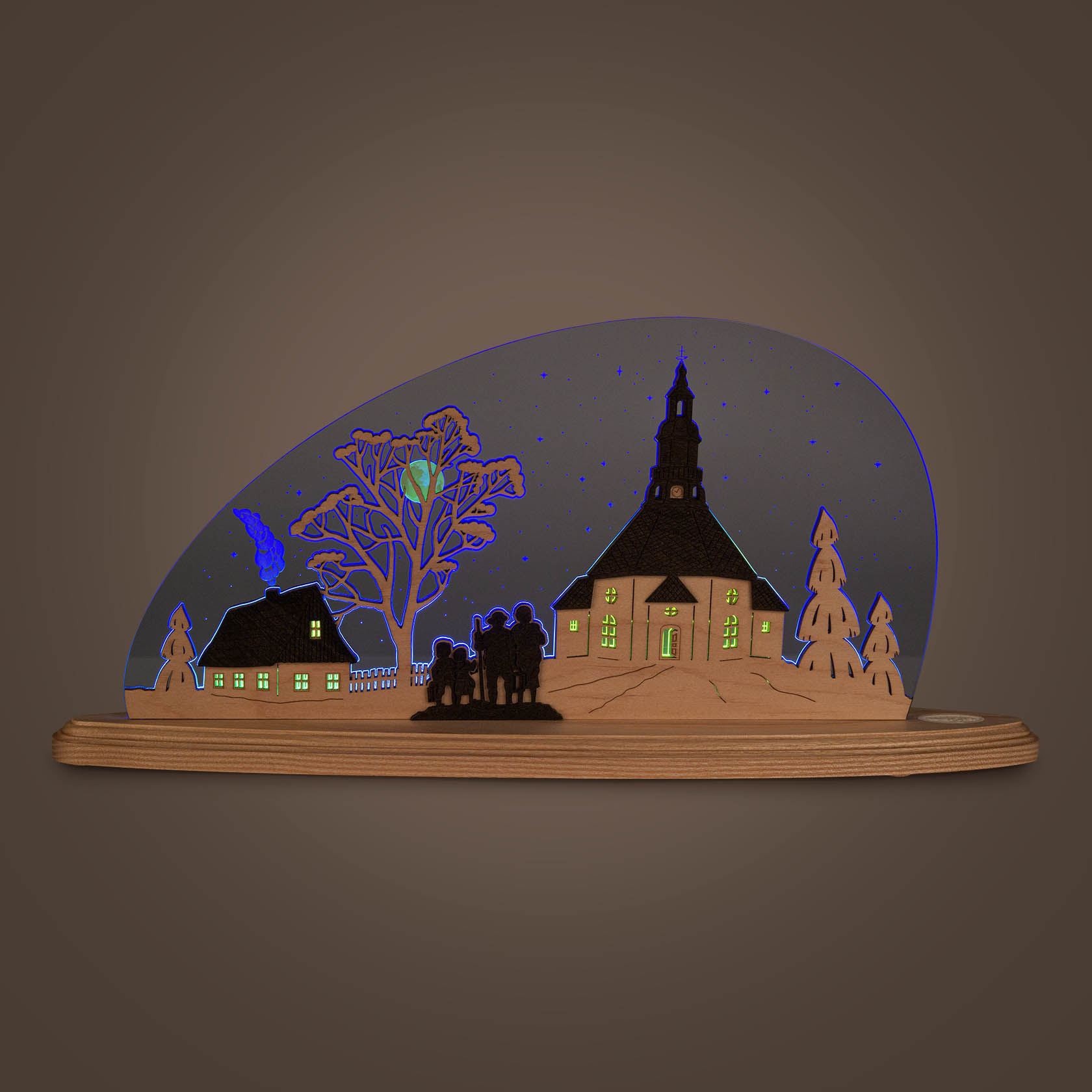 Beleuchtete Holzsilhouette mit Seiffener Kirche, in der Nacht. Die Fenster der Kirche und eines Hauses leuchten gelb, umgeben von Bäumen und Besuchern.