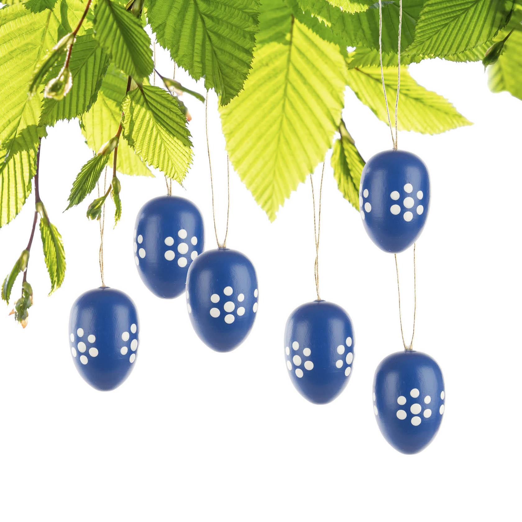 Sechs blaue Ostereier mit weißem Punktmuster hängen an grünen Zweigen.