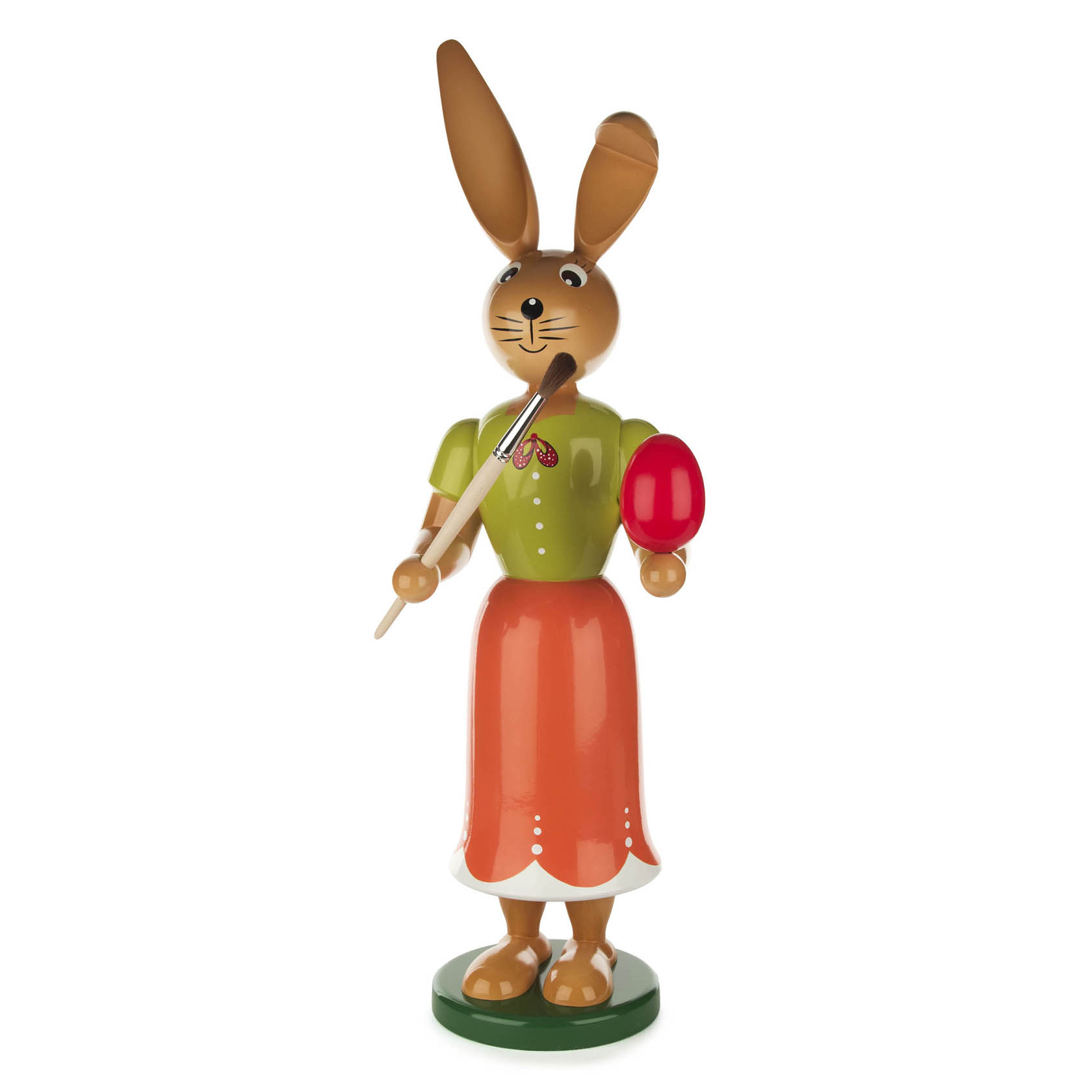Holzfigur einer stehenden Hasenmalerin. Sie trägt eine grüne Bluse, roten Rock und hält einen Pinsel sowie ein rotes Osterei.