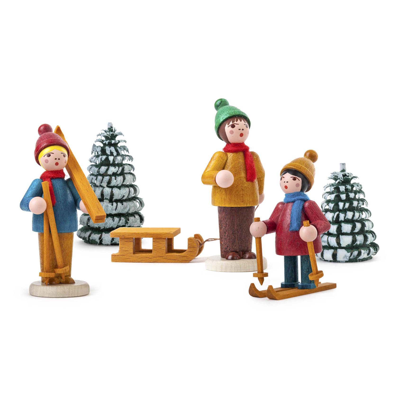 Drei farbig lasierte Holzfiguren als Wintersportler: ein Kind mit Skiern, eines mit Schlittschuhen und ein weiteres mit einem Schlitten vor zwei verschneiten Bäumen. im Dregeno Online Shop günstig kaufen