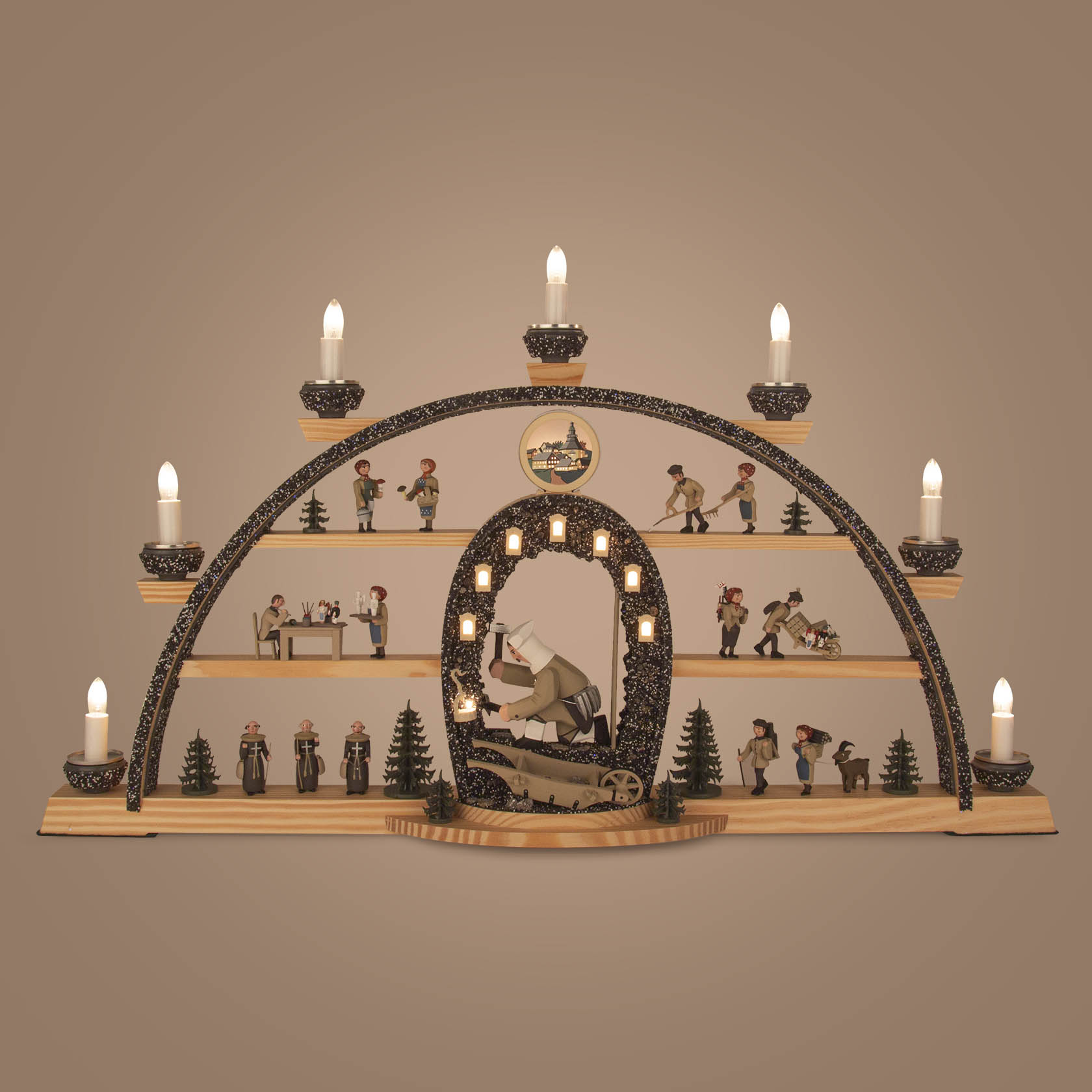 A miner's illuminated arch with miners, a miner statue holding a lamp, and small decorative trees. It is adorned with lit candles on top.