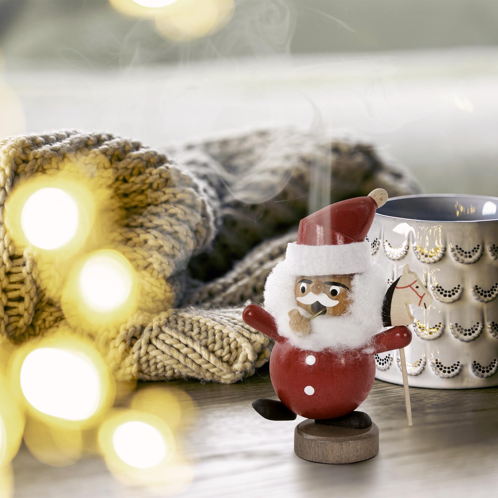 Ein Mini-Räuchermann in Form eines Weihnachtsmannes tanzt auf einem Tisch. Er trägt einen roten Mantel, Mütze und hat einen Weihnachtsbaum in der Hand.