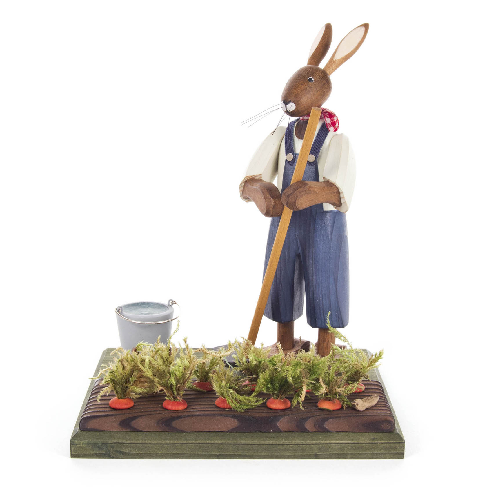 Eine hölzerne Hasenfigur in blauer Latzhose und weißem Hemd steht mit einer Hacke in einem Möhrenfeld, neben einem silbernen Eimer. im Dregeno Online Shop günstig kaufen